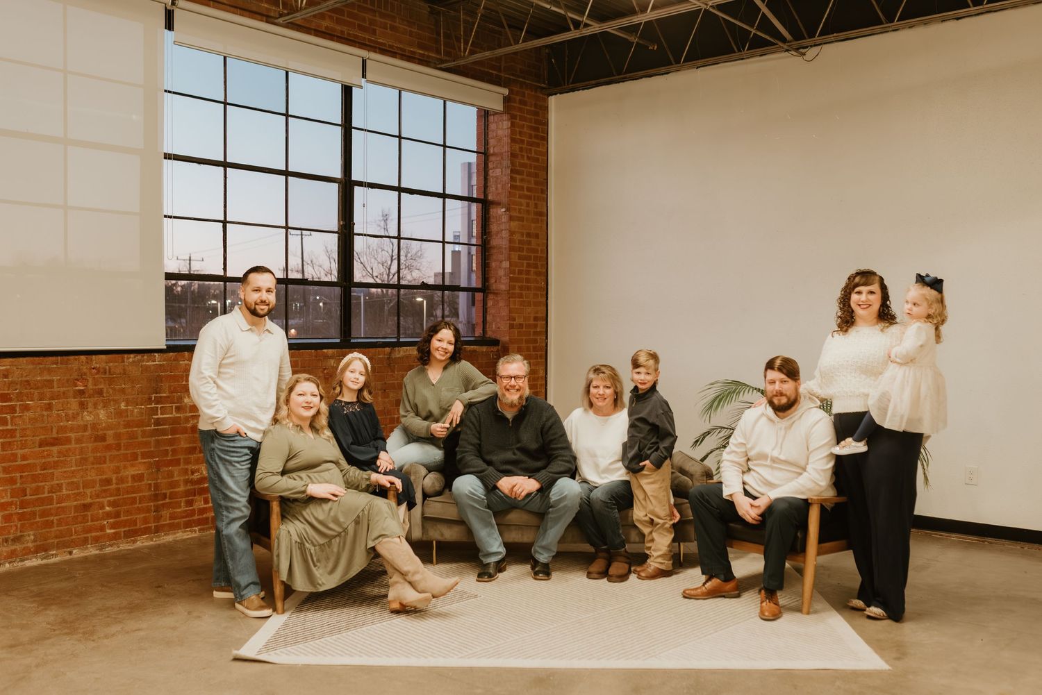 Large group of ten coworkers posing together in a bright industrial brick studio space.