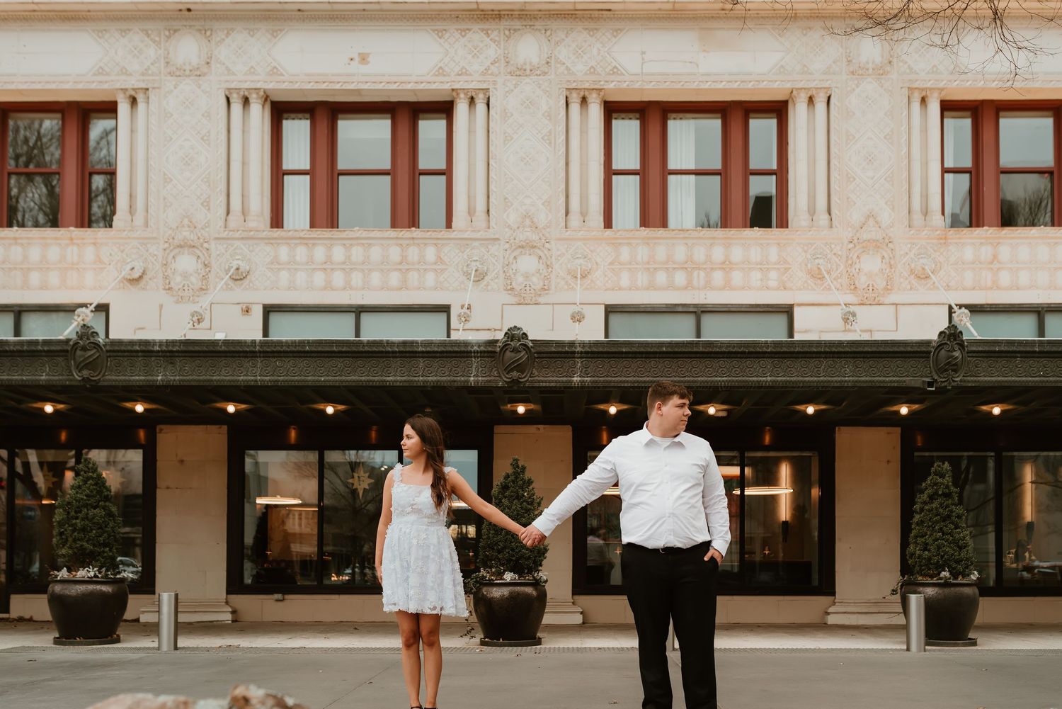 Couple holding hands in front of an ornate historic building facade during an engagement photo session.