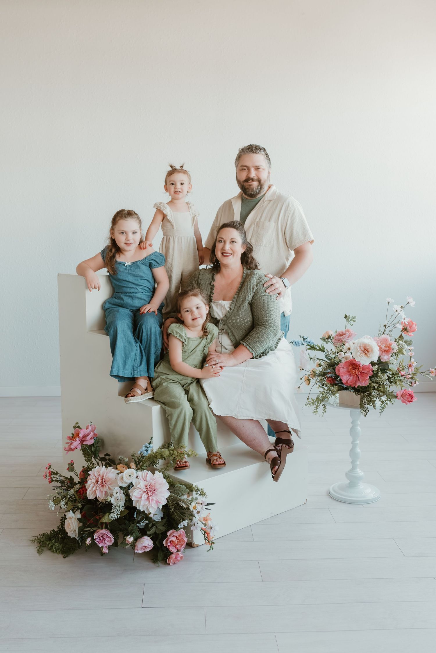 Family of five poses with pink and white floral arrangements in bright white photography studio.