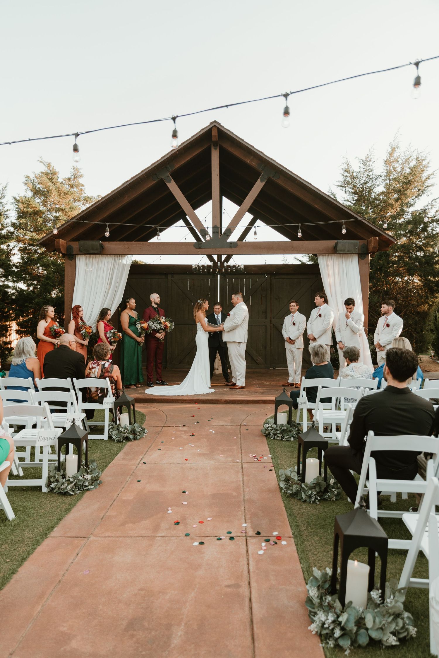 Couple exchanging vows under rustic wooden pavilion at outdoor wedding ceremony at golden hour.