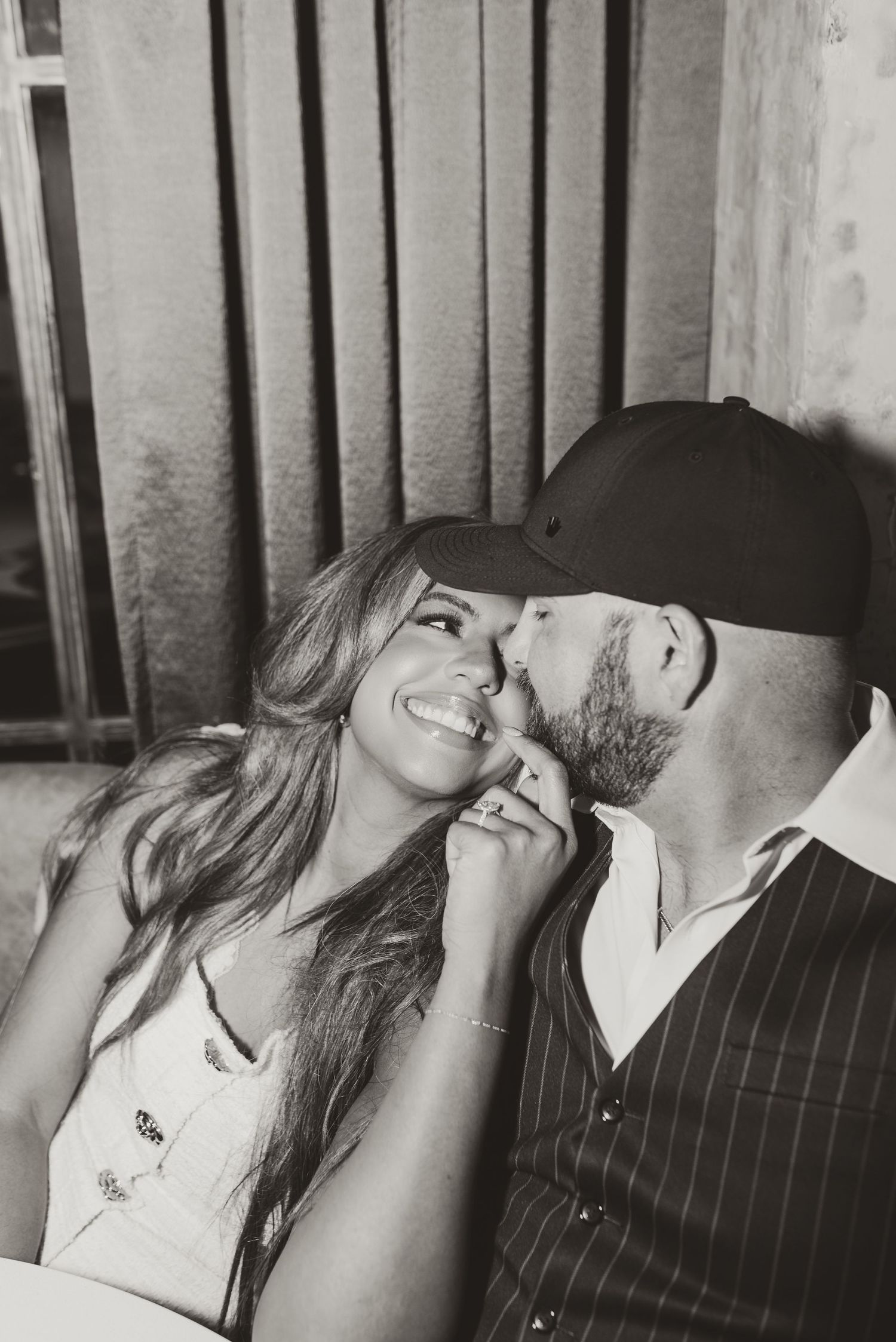 Black and white romantic couple photo with man kissing womans cheek as she smiles joyfully.