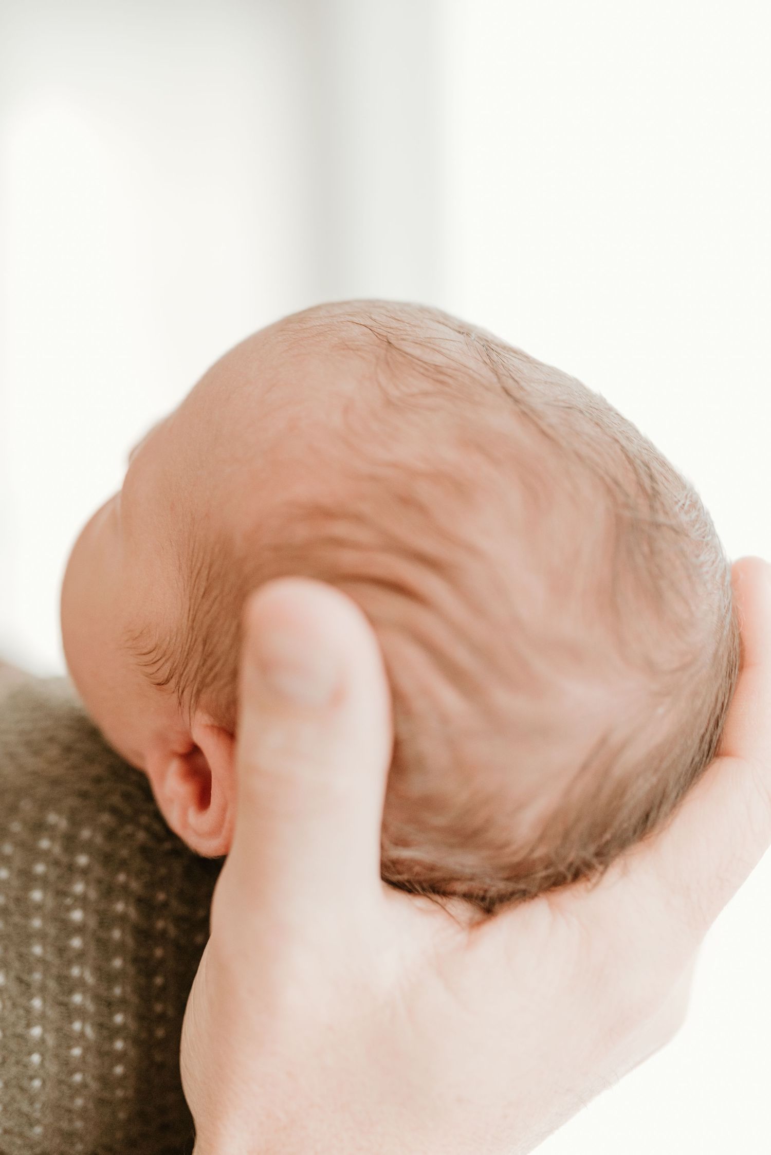 A close-up of a parent's hand gently cradling the back of a sleeping newborn baby's head.