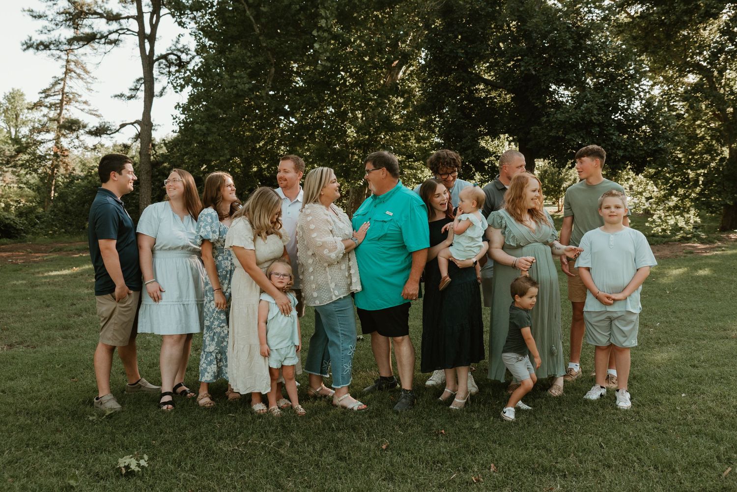 Large extended family group portrait outdoors on green grass with trees in background.