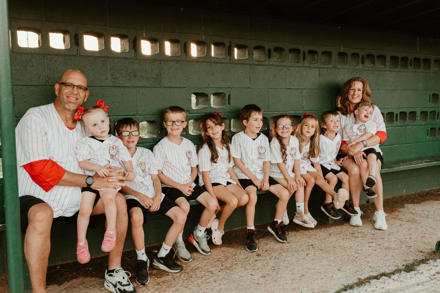 Large family posing together in a baseball dugout, wearing white jerseys, smiling for a group photo.