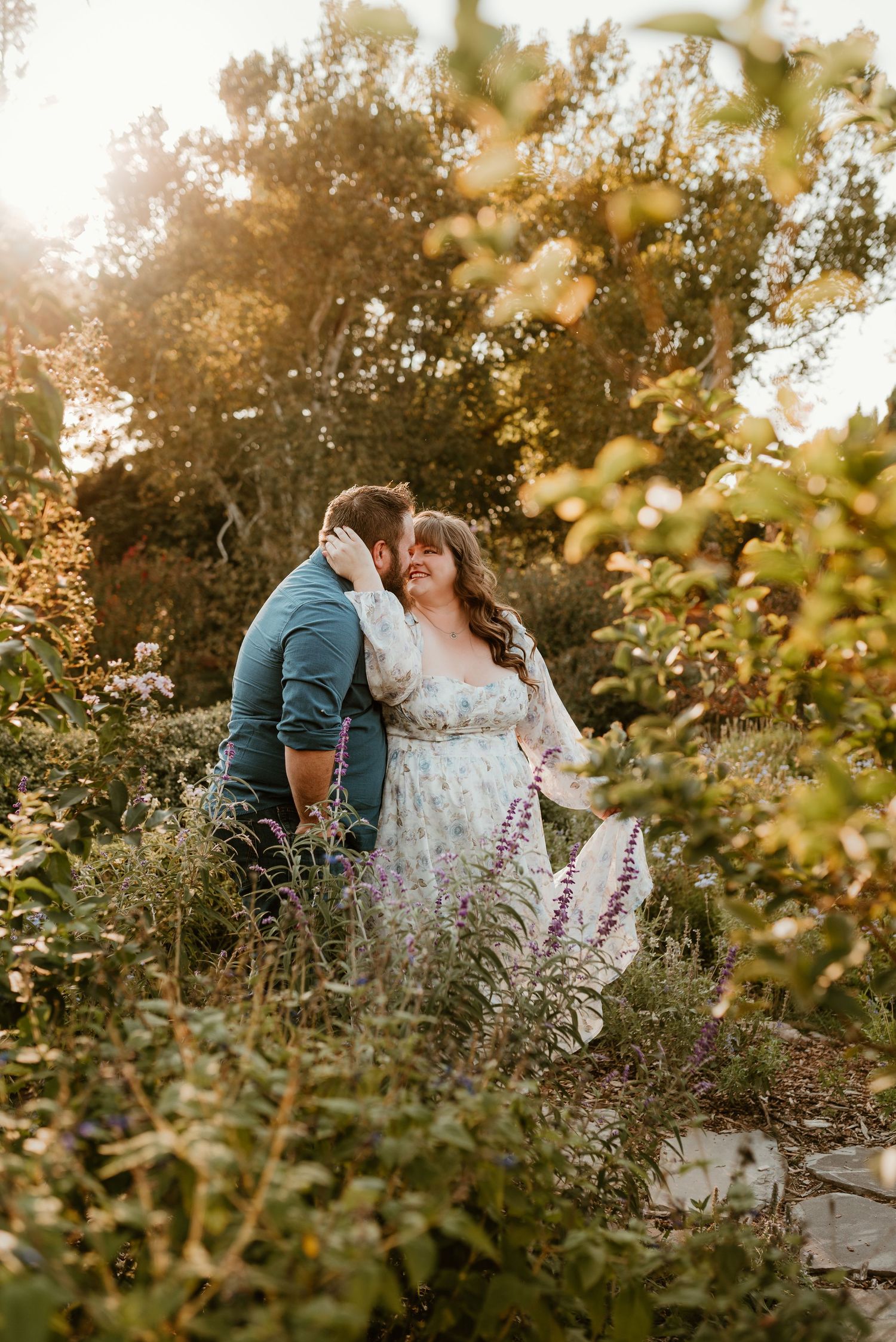 Couple sharing a romantic moment surrounded by lush greenery and golden sunlight in a garden.