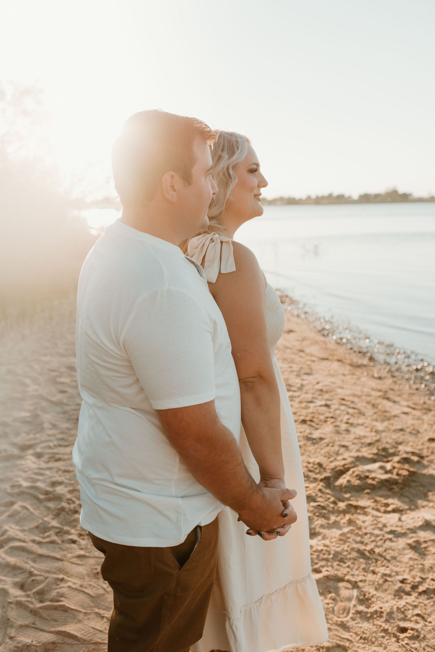 Couple holding hands on a sandy beach at golden hour sunset.