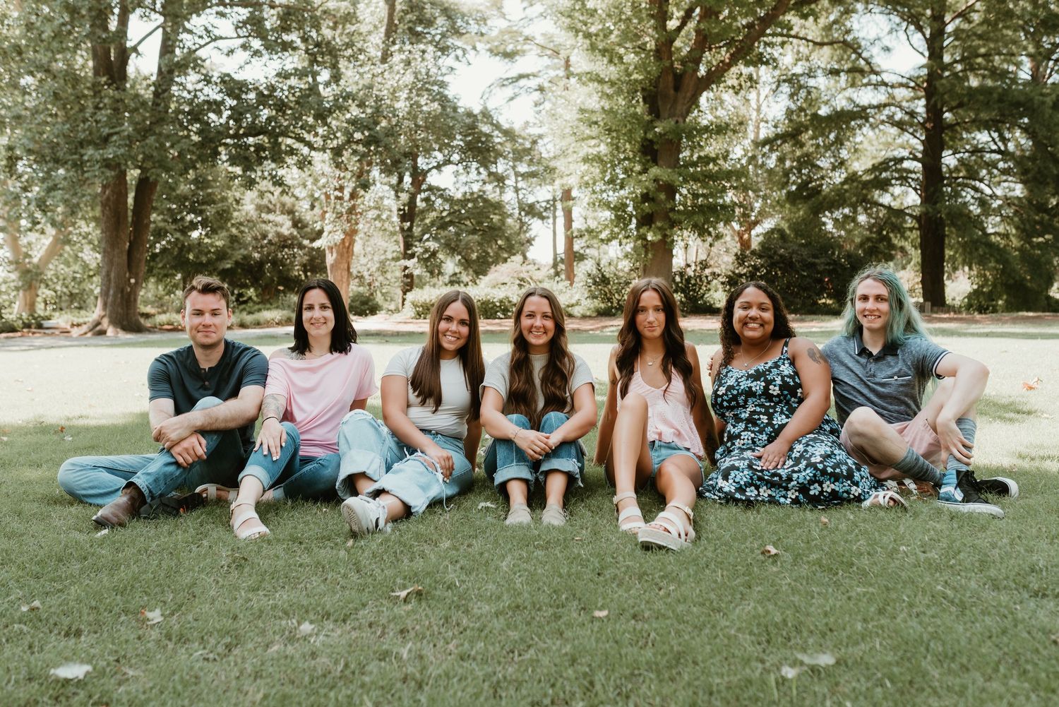Seven family members sitting together on green grass in a park, smiling for a portrait.