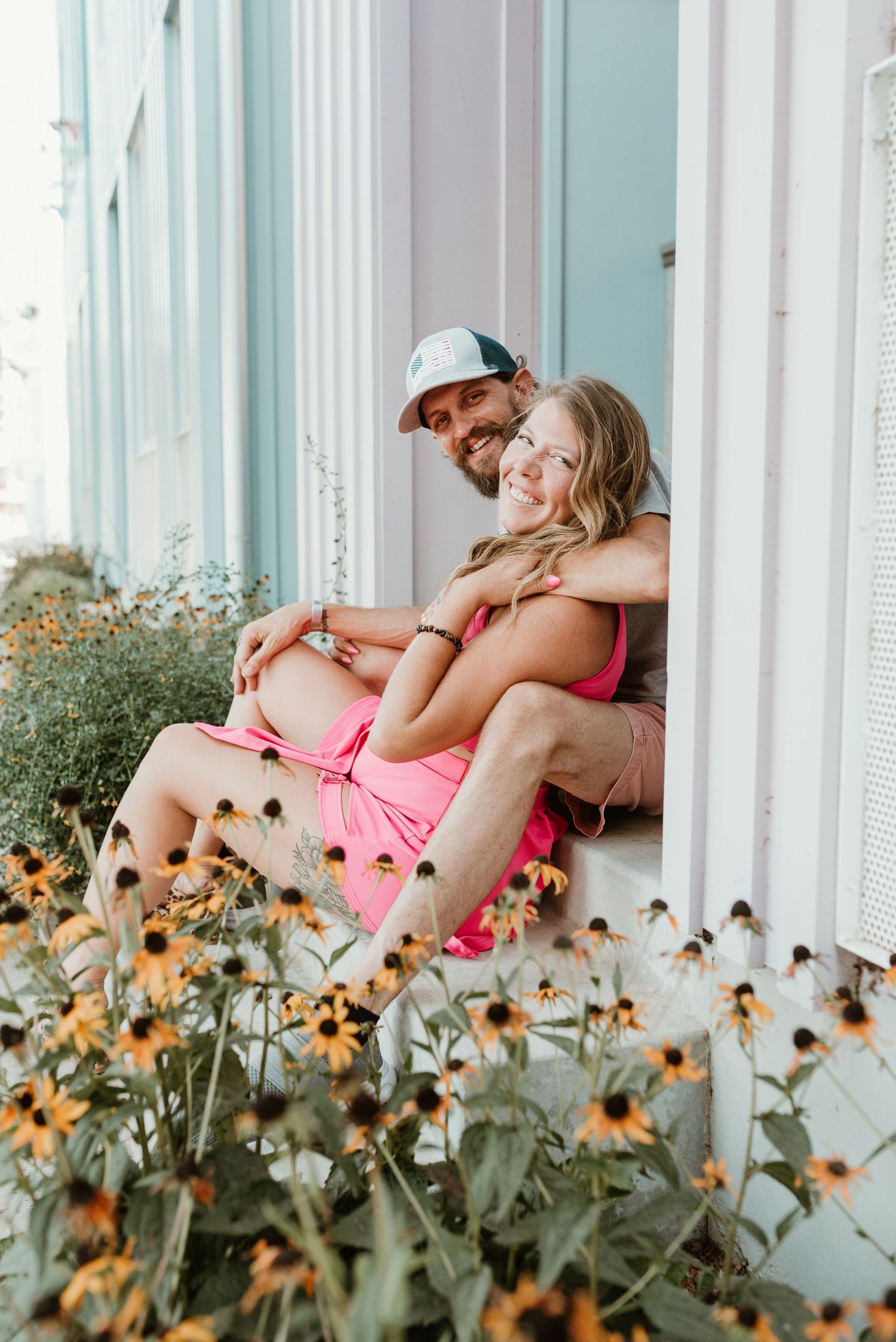 Smiling couple sitting together in a window surrounded by blooming black-eyed Susan flowers.
