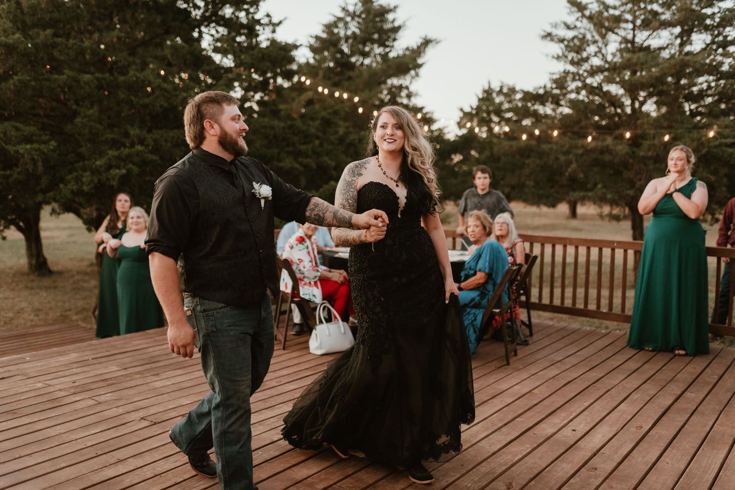 Bride and groom sharing first dance on wooden deck at outdoor wedding reception at dusk.