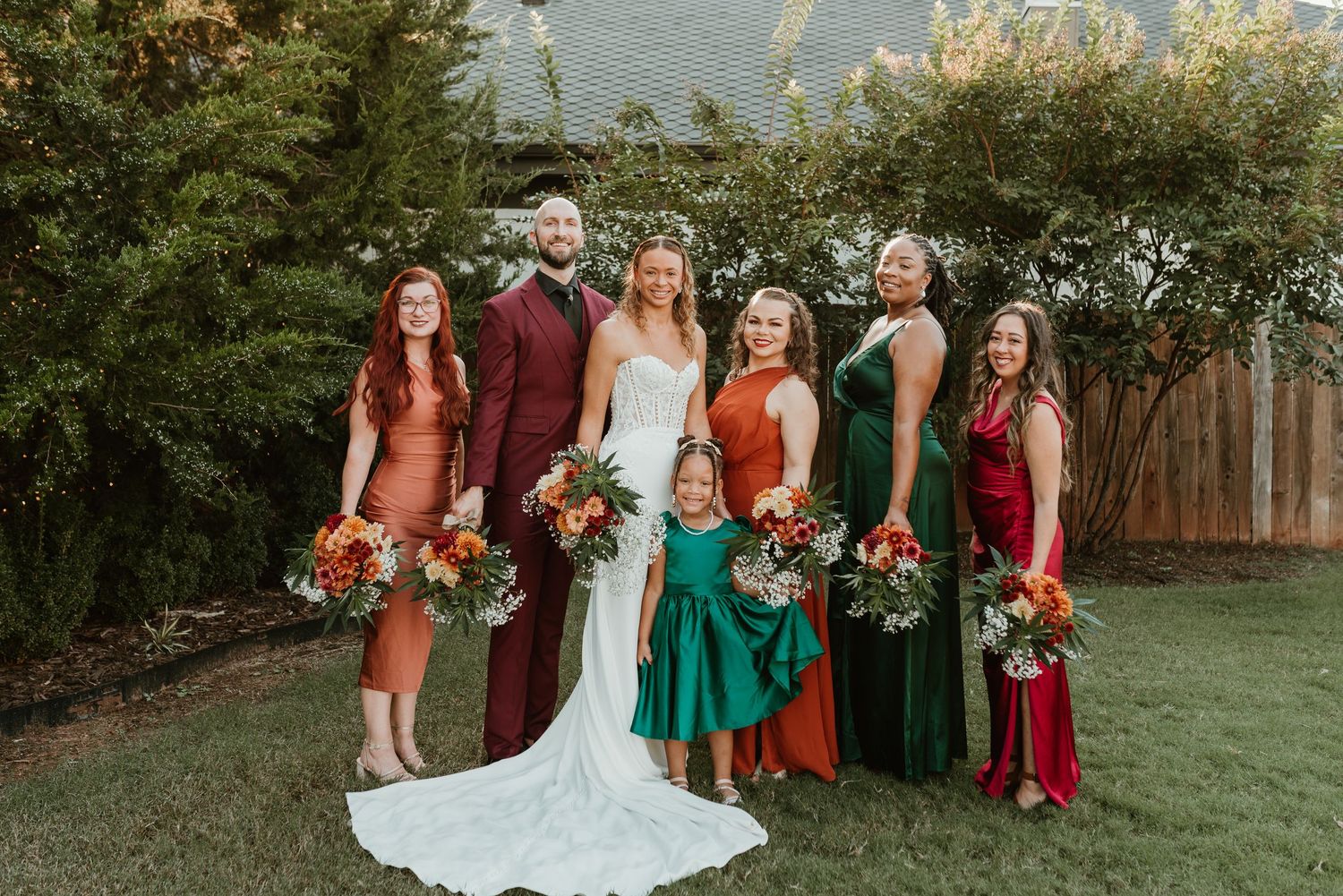 Bride in white gown with colorful bridal party in autumn-toned dresses holding vibrant bouquets.
