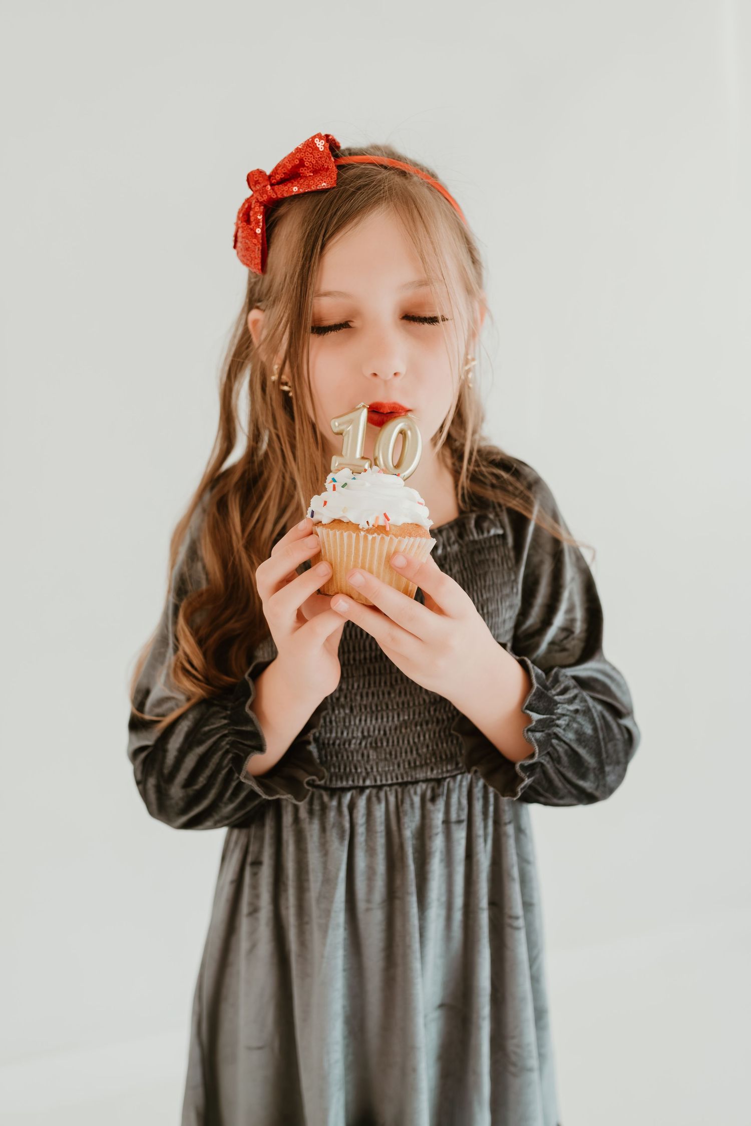 Young girl in velvet dress blowing out candles on a cupcake with number 10 topper.
