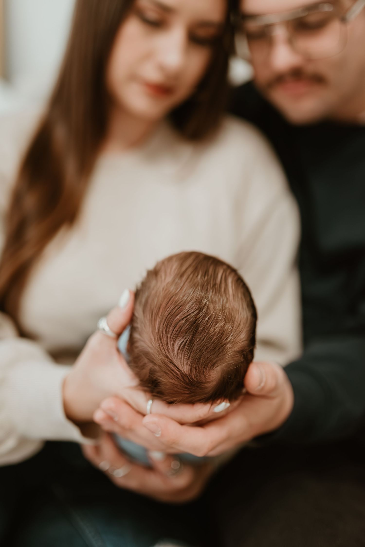 New parents gazing lovingly at their newborn baby's head cradled gently in their hands.