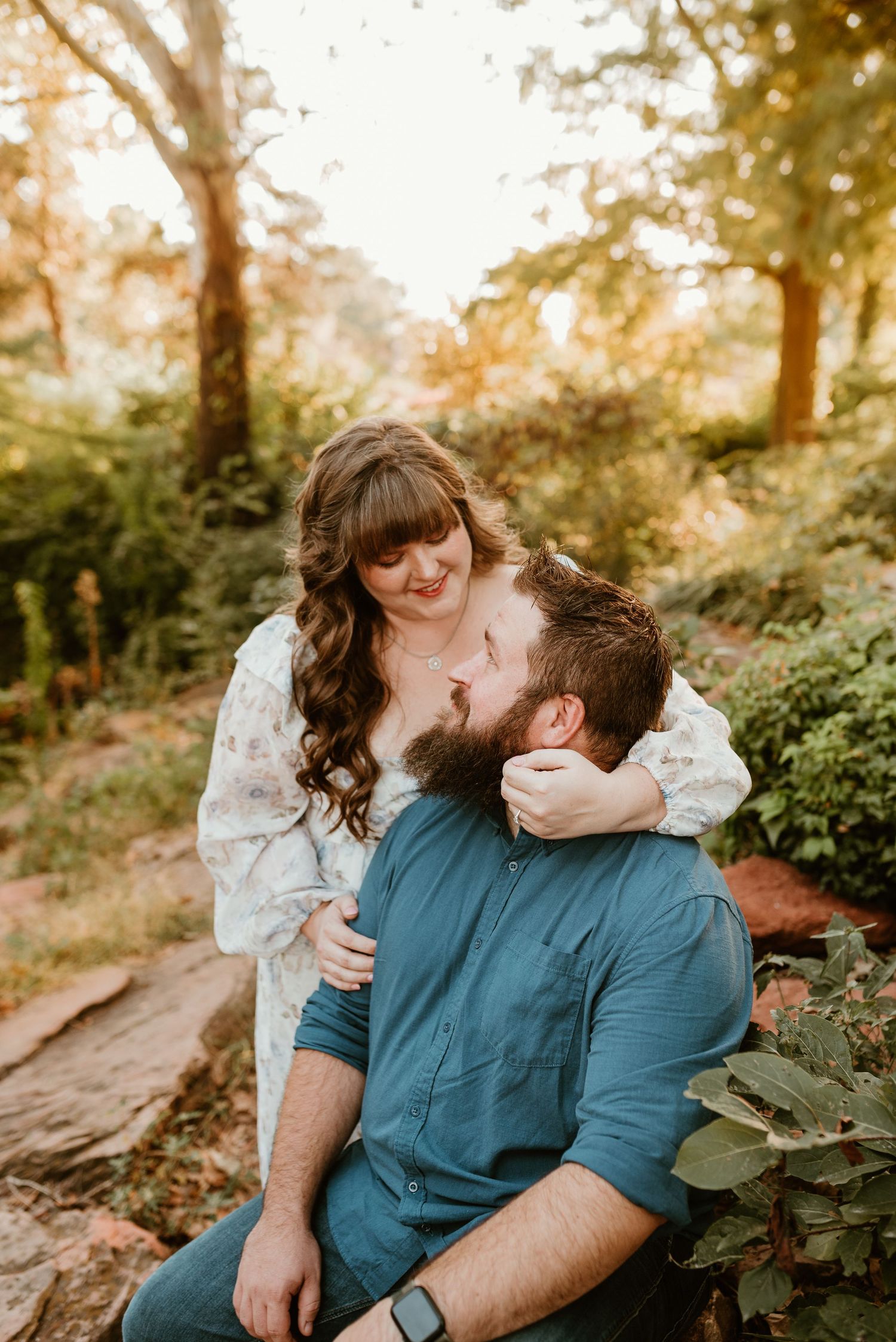 A woman in a floral dress tenderly holds a bearded mans face while sitting outdoors.