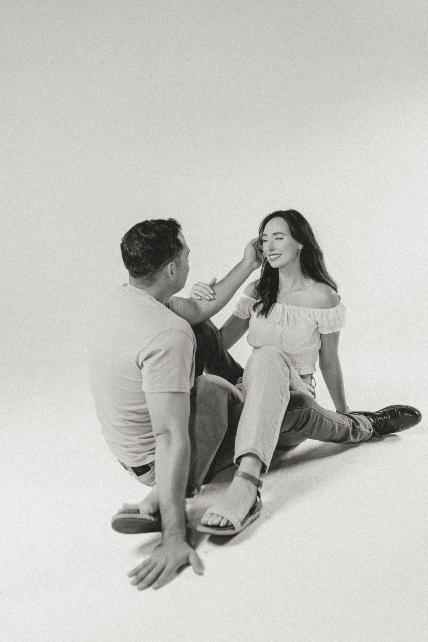 Black and white photo of couple sitting on floor, man gently touching womans hair.