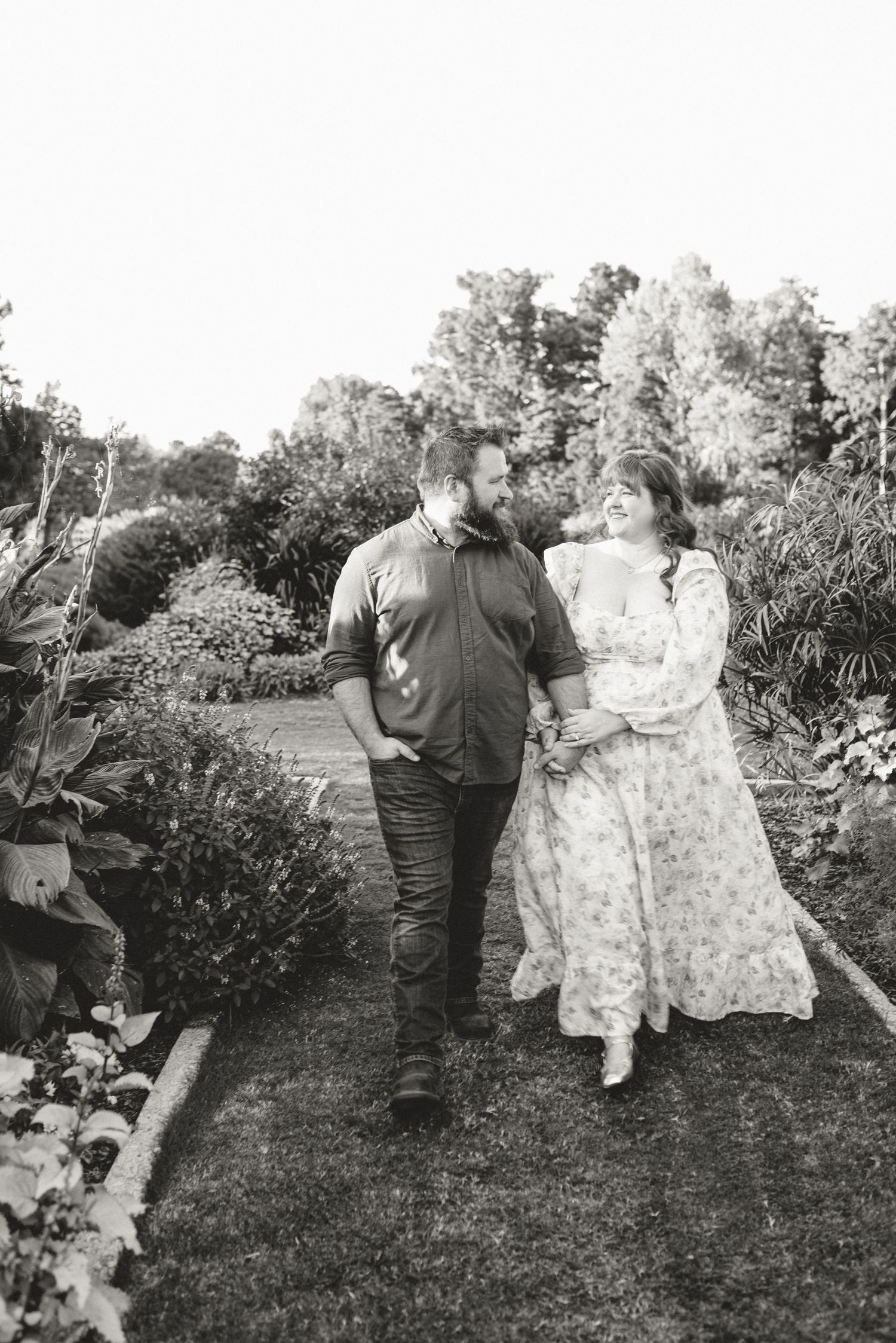 Black and white photo of a smiling couple walking together through a lush garden path.
