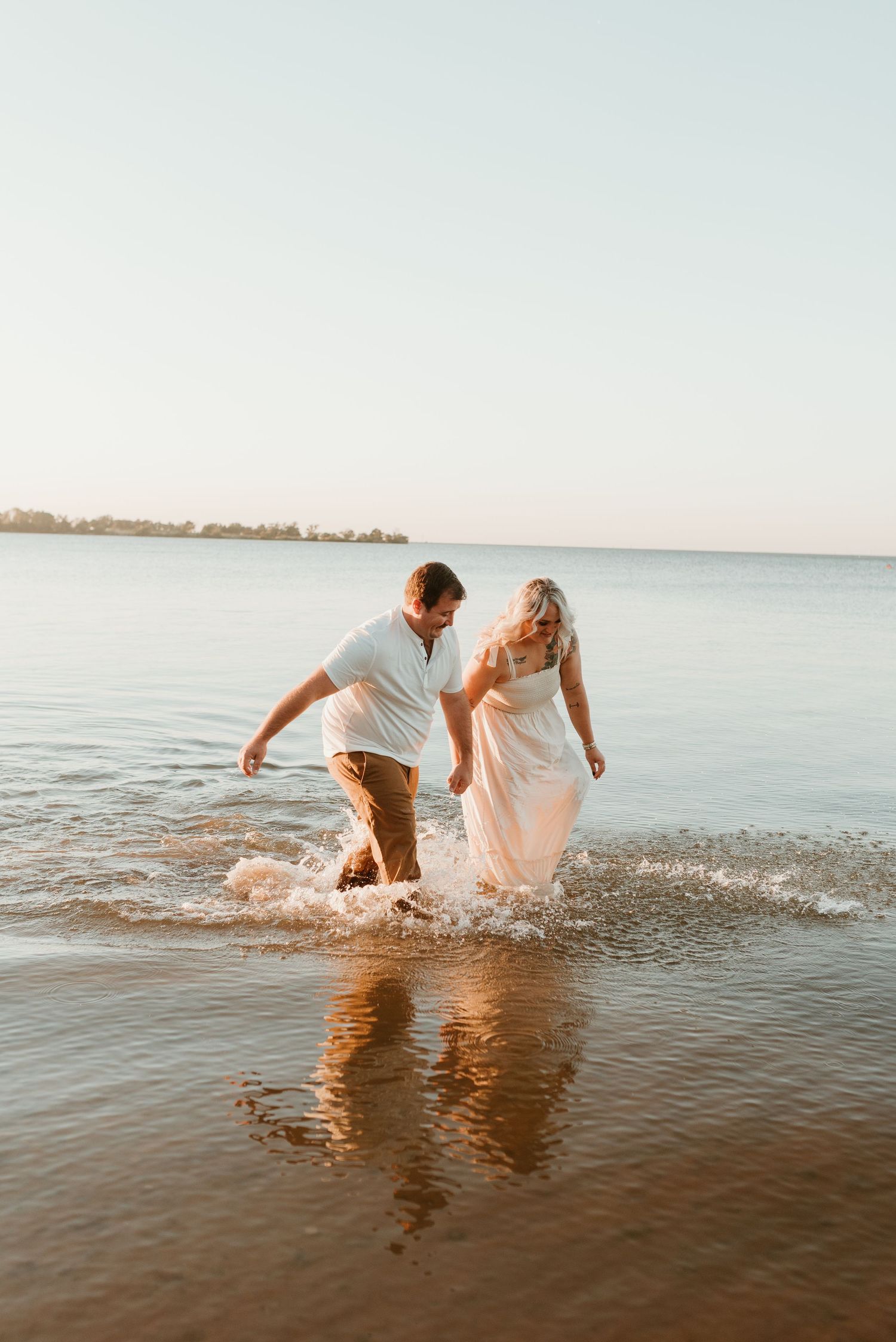 Joyful couple splashing through shallow water at the beach during golden hour.