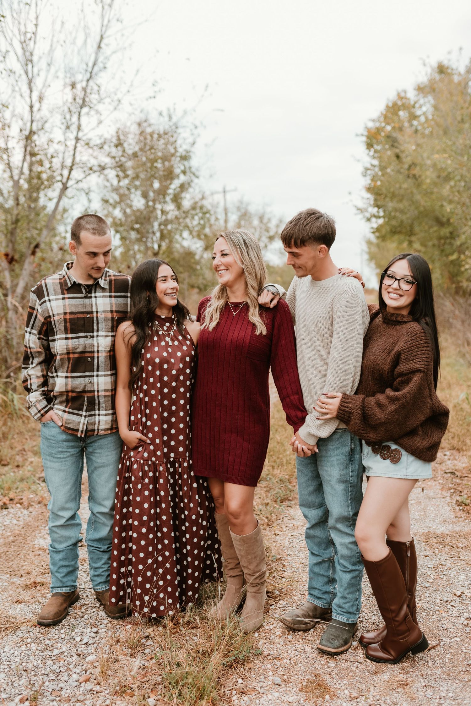 Family of five posing outdoors in autumn, wearing coordinated earth-tone outfits on a rustic path.