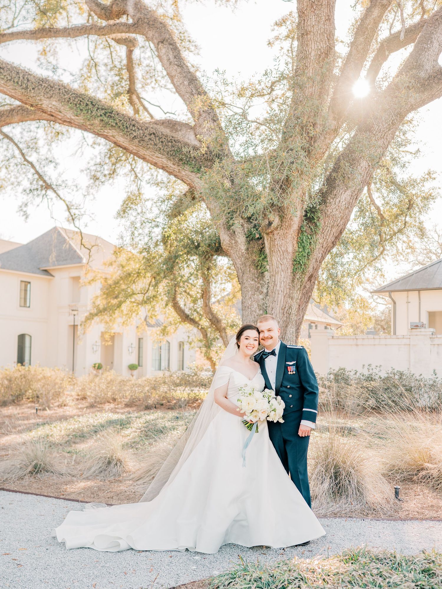 A couple poses together under sunlit oak trees in a romantic outdoor wedding photoshoot.