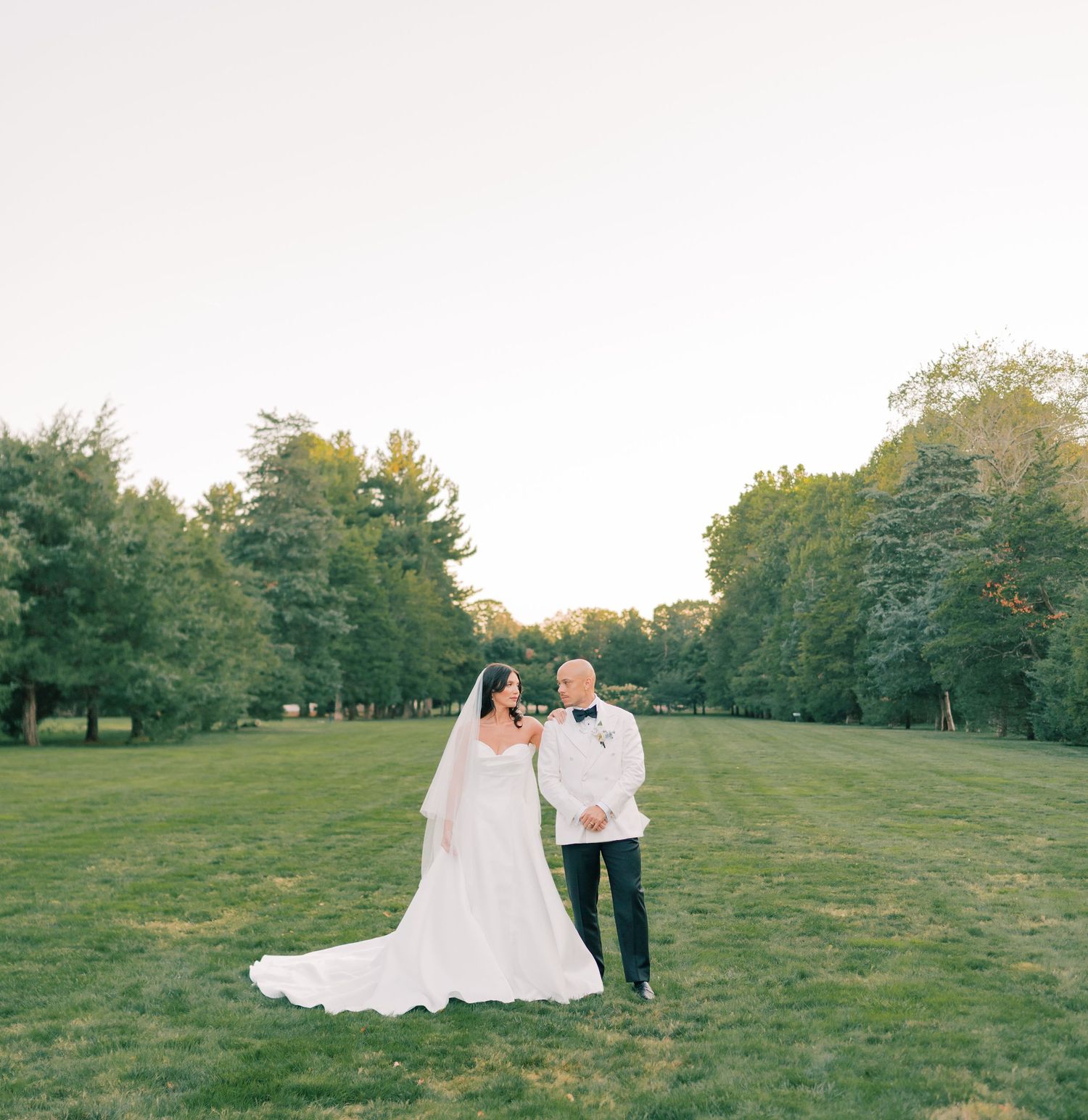 Couple walking together on a grassy hillside during golden hour with trees in the background.