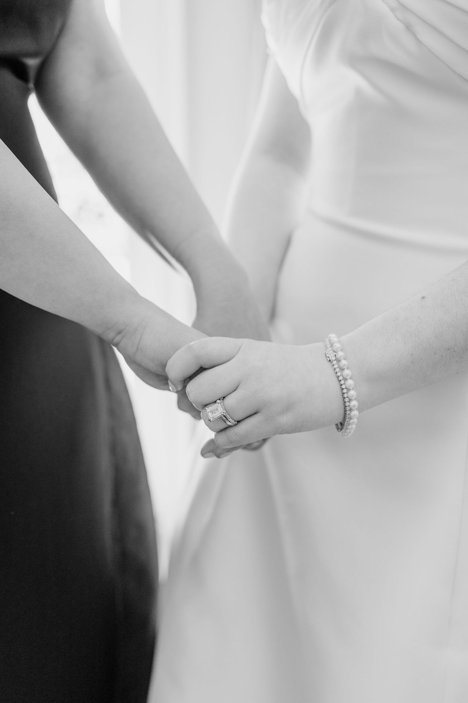 A close-up detail shot of a bride's hand wearing an elegant diamond wedding ring against a white dress background.