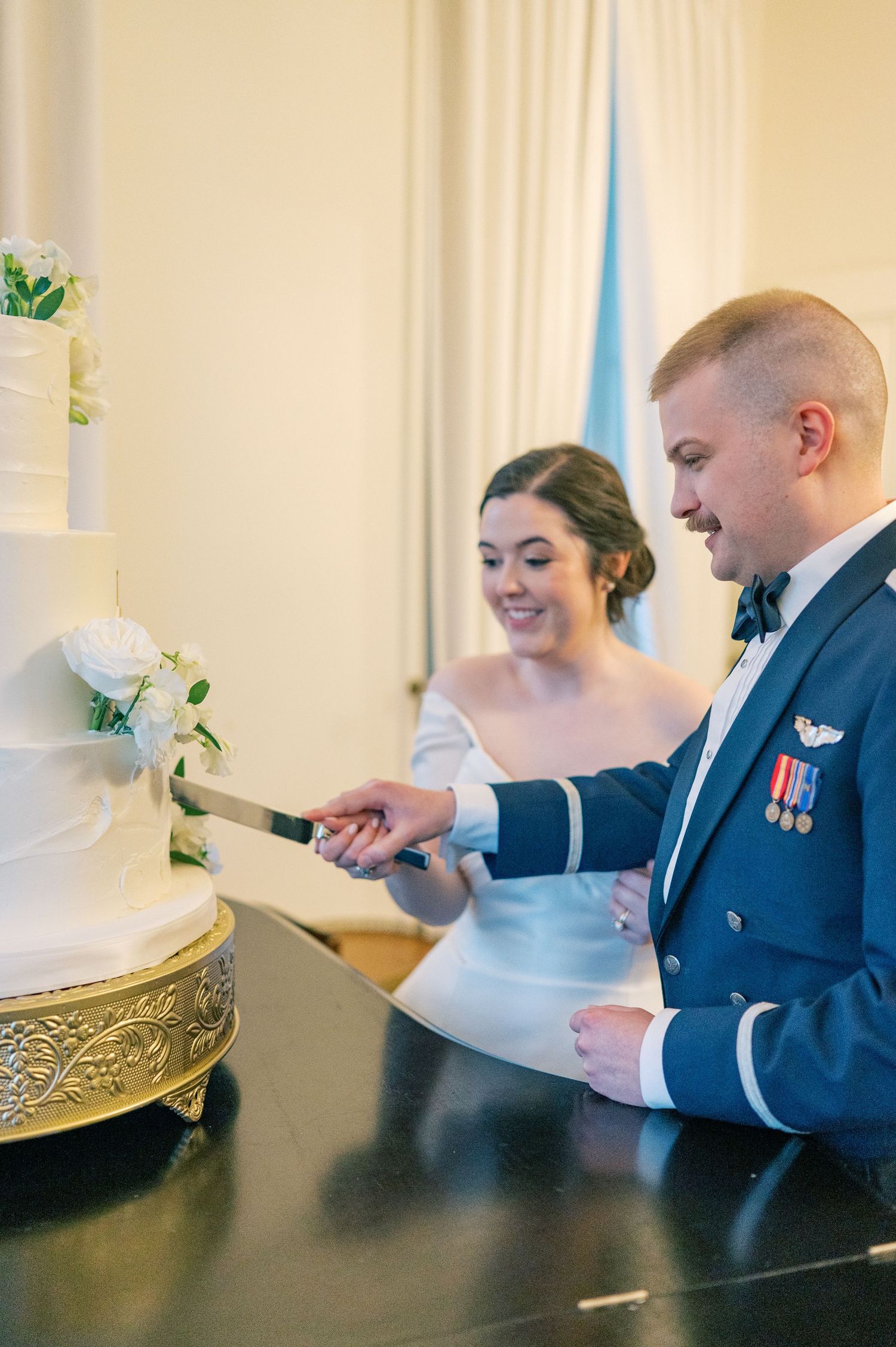Couple in formal attire sits at a table during their wedding signing documents together in a bright room.