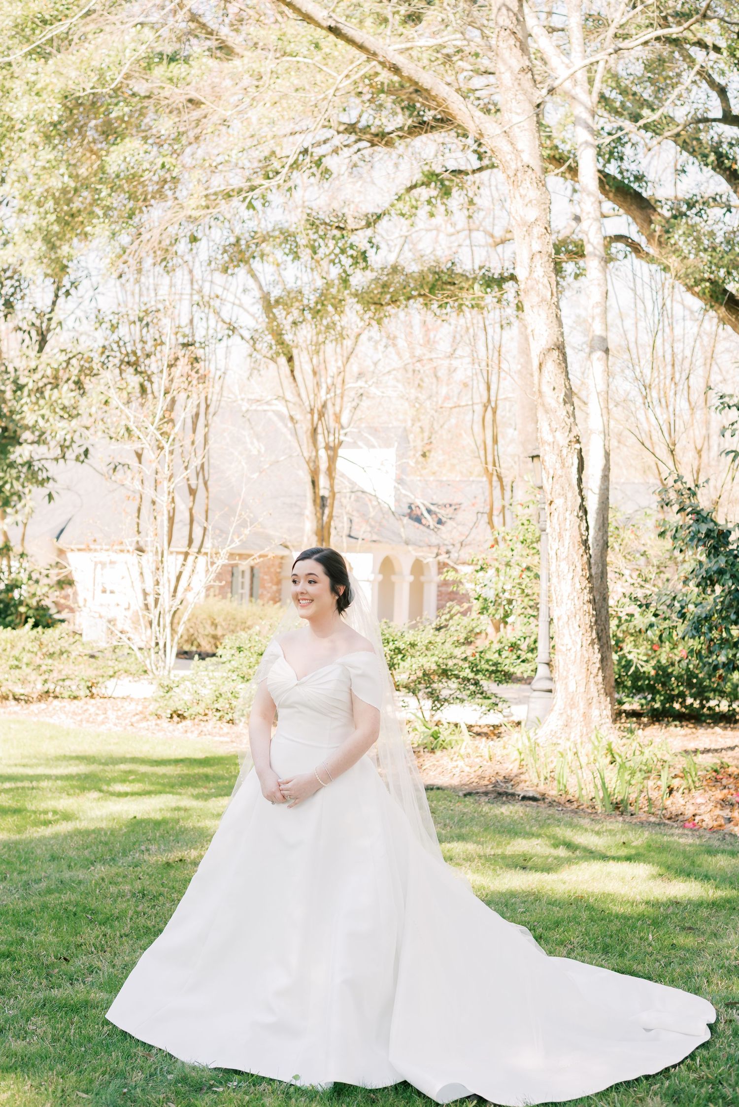 A bride in a flowing white ballgown poses gracefully in a sunlit garden setting during a spring wedding photoshoot.