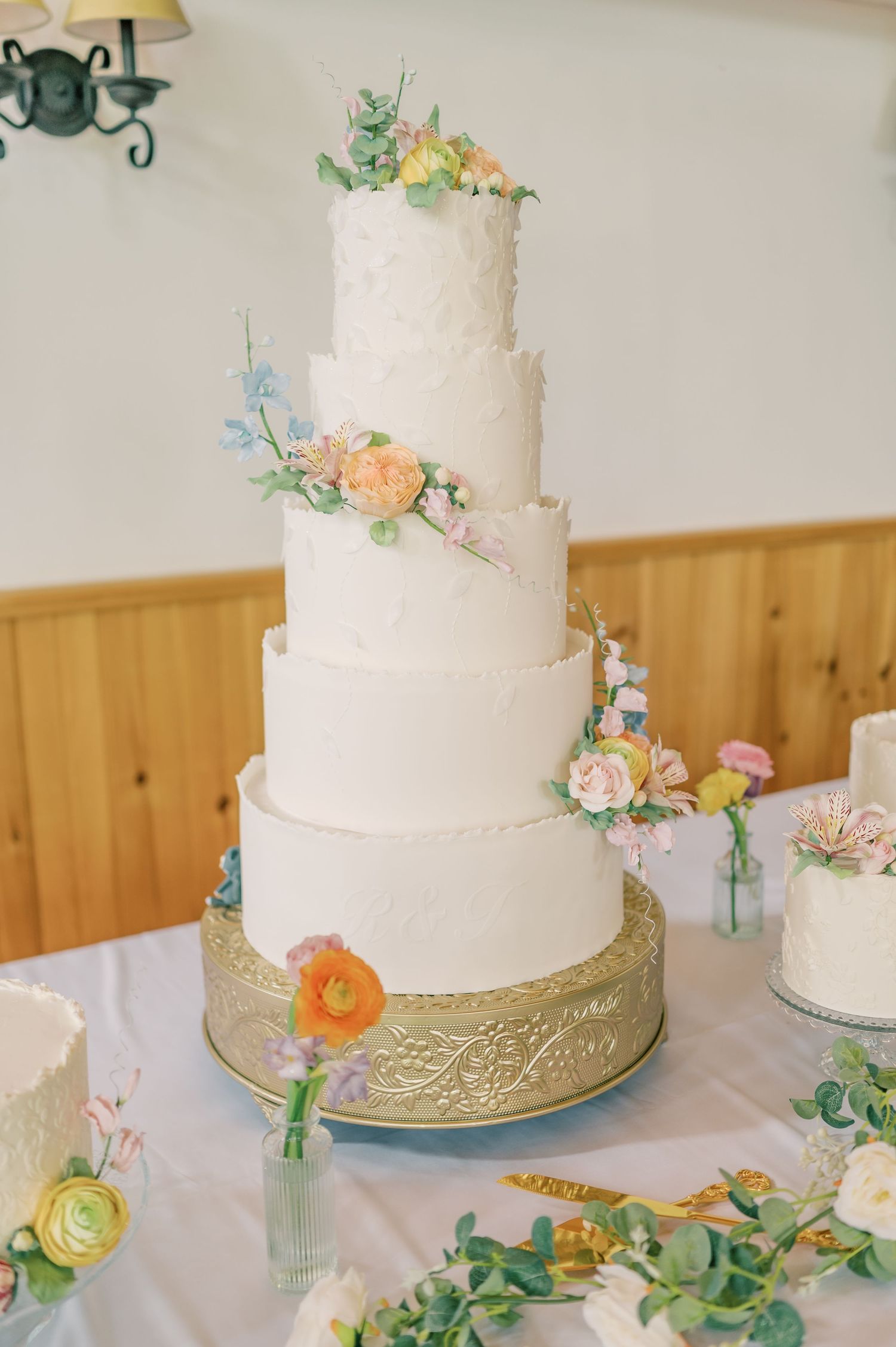 Elegant white wedding cake adorned with delicate pastel flowers and greenery on a gold cake stand.