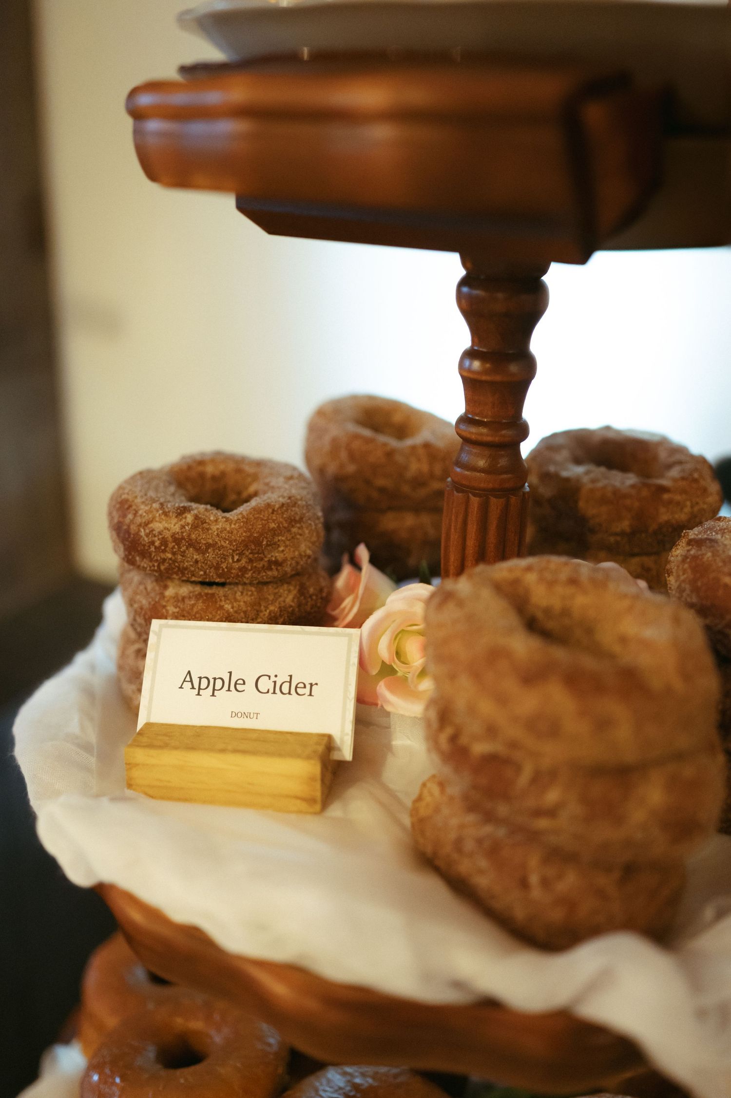 Fresh apple cider donuts dusted with cinnamon sugar displayed on rustic wooden cake stands with label cards.
