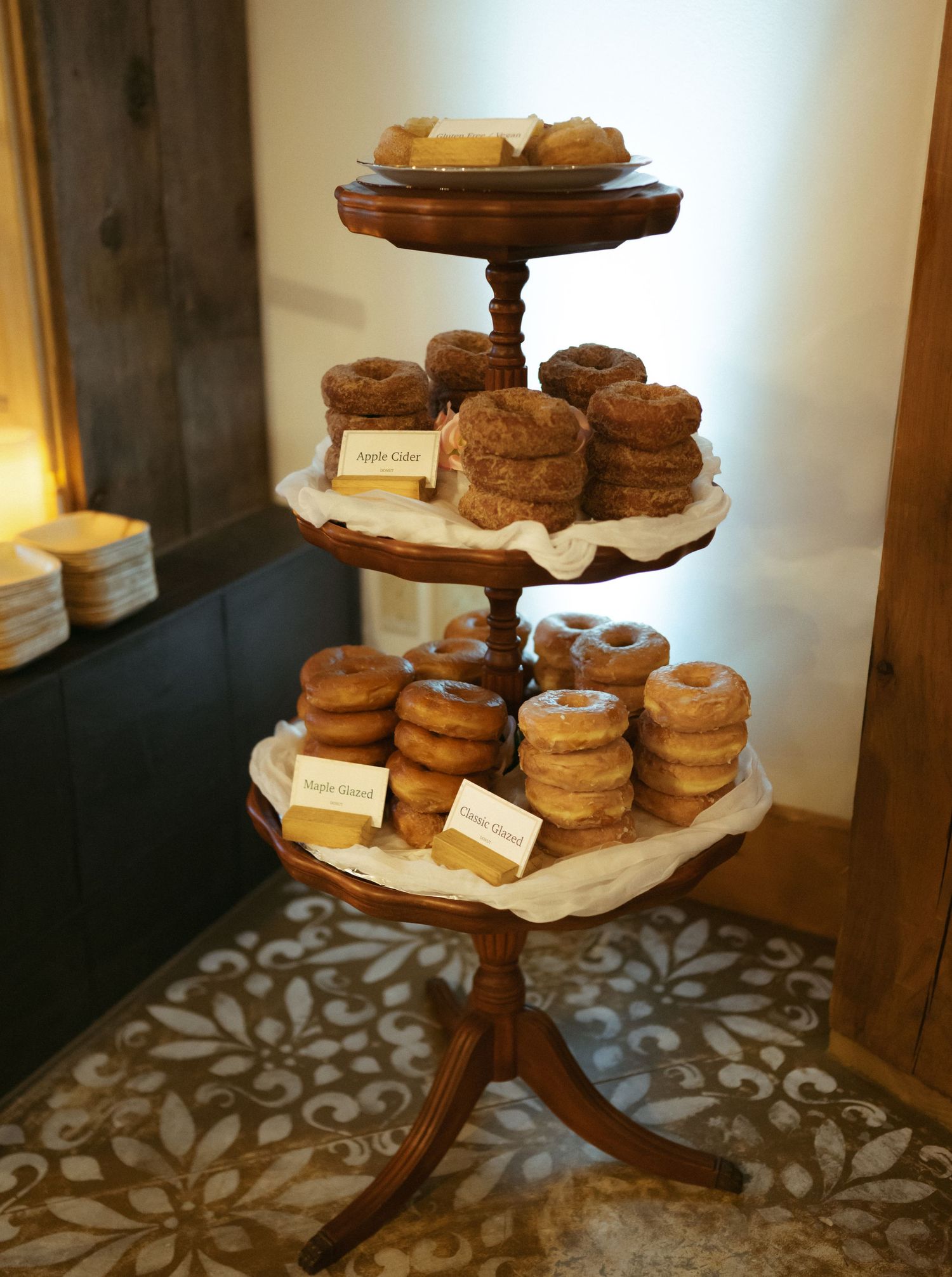 A three-tiered wooden display stand filled with stacks of fresh donuts on parchment paper.