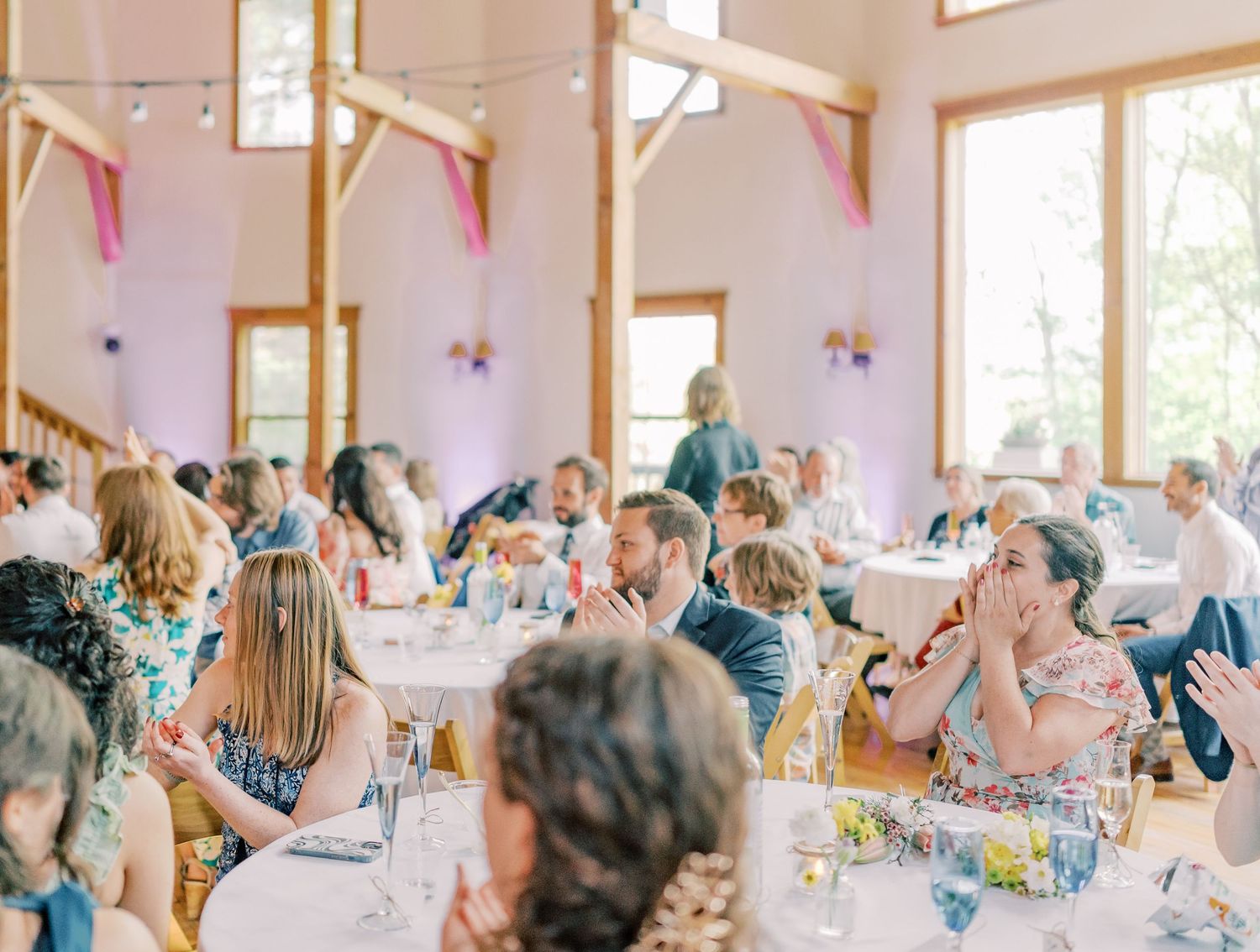 Wedding guests sit at decorated reception tables with pink and blue decor while enjoying a meal together.