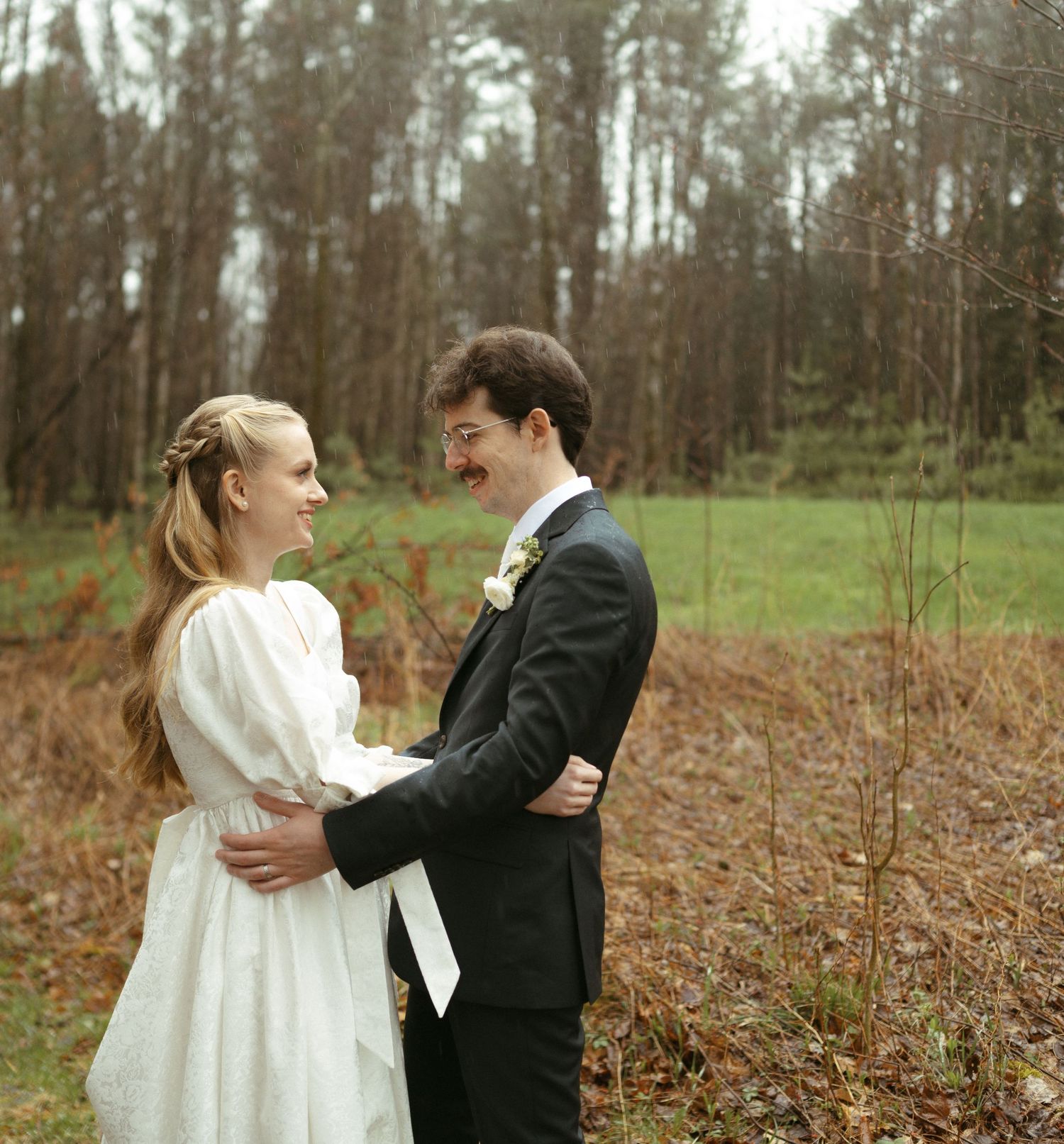A couple in wedding attire share an intimate moment together in a wooded forest setting.