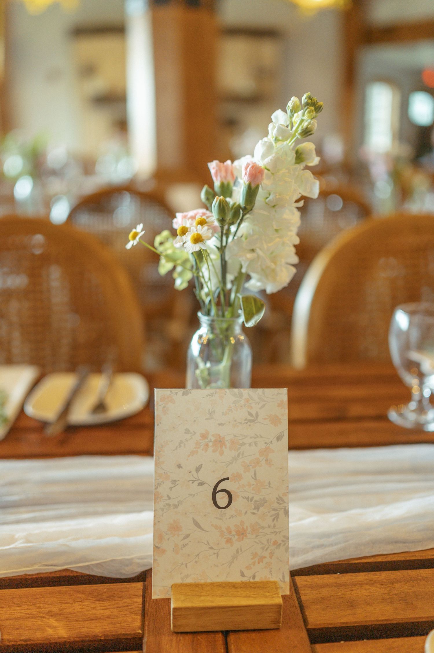 Table number card and small floral centerpiece in mason jar at rustic wedding reception setup.