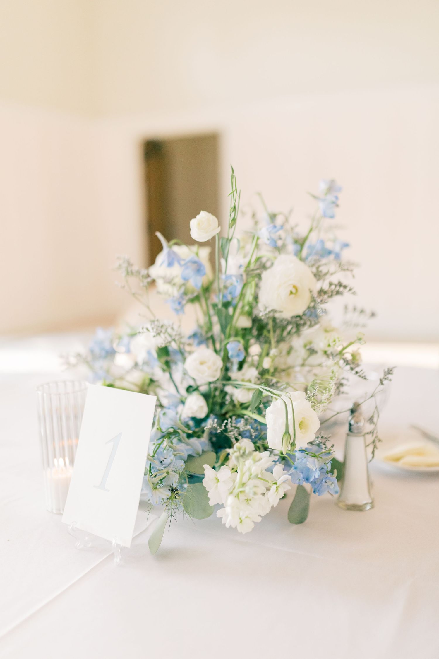 Elegant white and blue floral centerpiece arrangements on a light tablecloth with delicate place cards at a wedding reception.