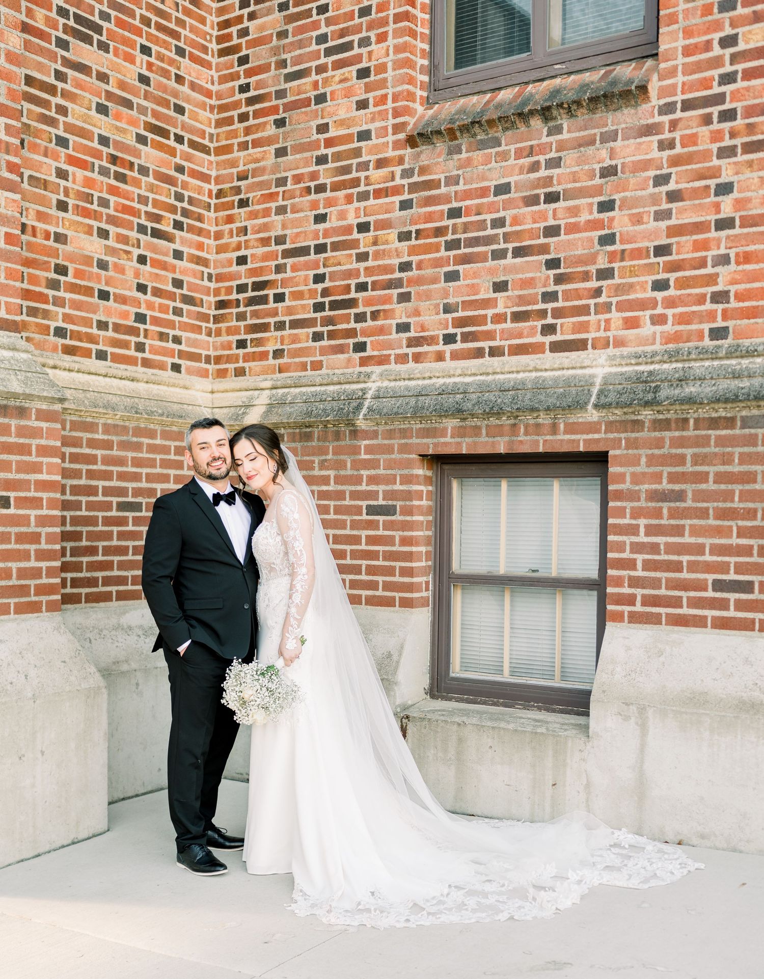 A couple shares romantic moments in front of a brick building during their wedding photo session.