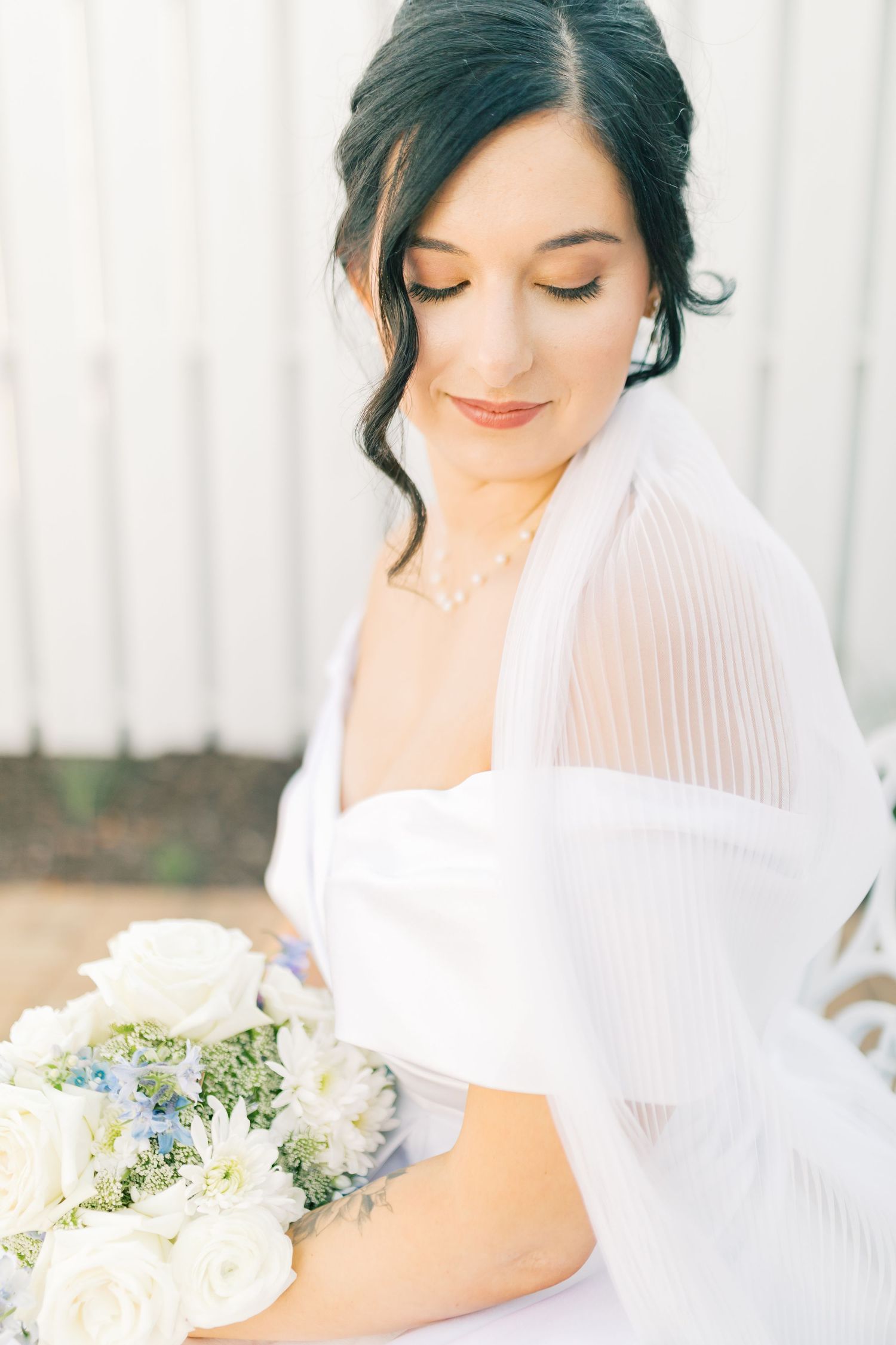 Elegant bridal portrait with soft white veil and delicate bouquet featuring cream roses and blue flowers.