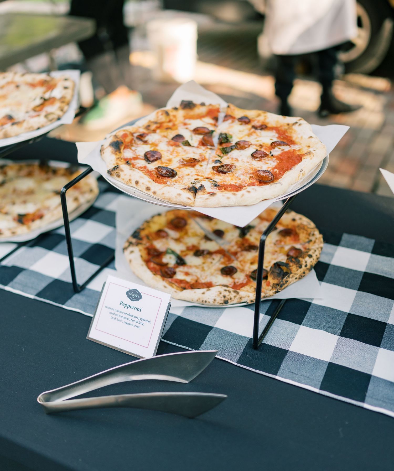 Artisanal wood-fired Neapolitan pizzas with various toppings displayed on a checkered tablecloth at a restaurant event.