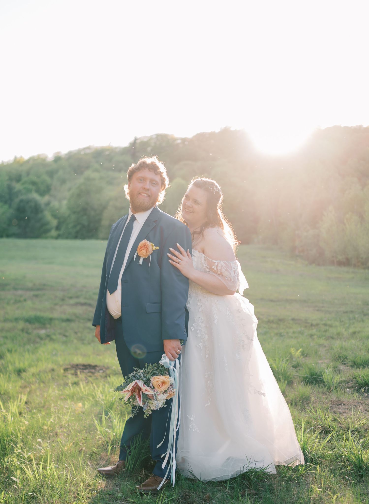 A couple poses together in a sunlit field during their wedding, with golden hour light creating a romantic atmosphere.