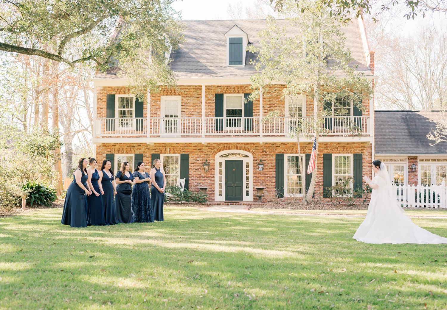 A panoramic view of a brick house exterior with a landscaped yard and formal group gathering on the lawn.