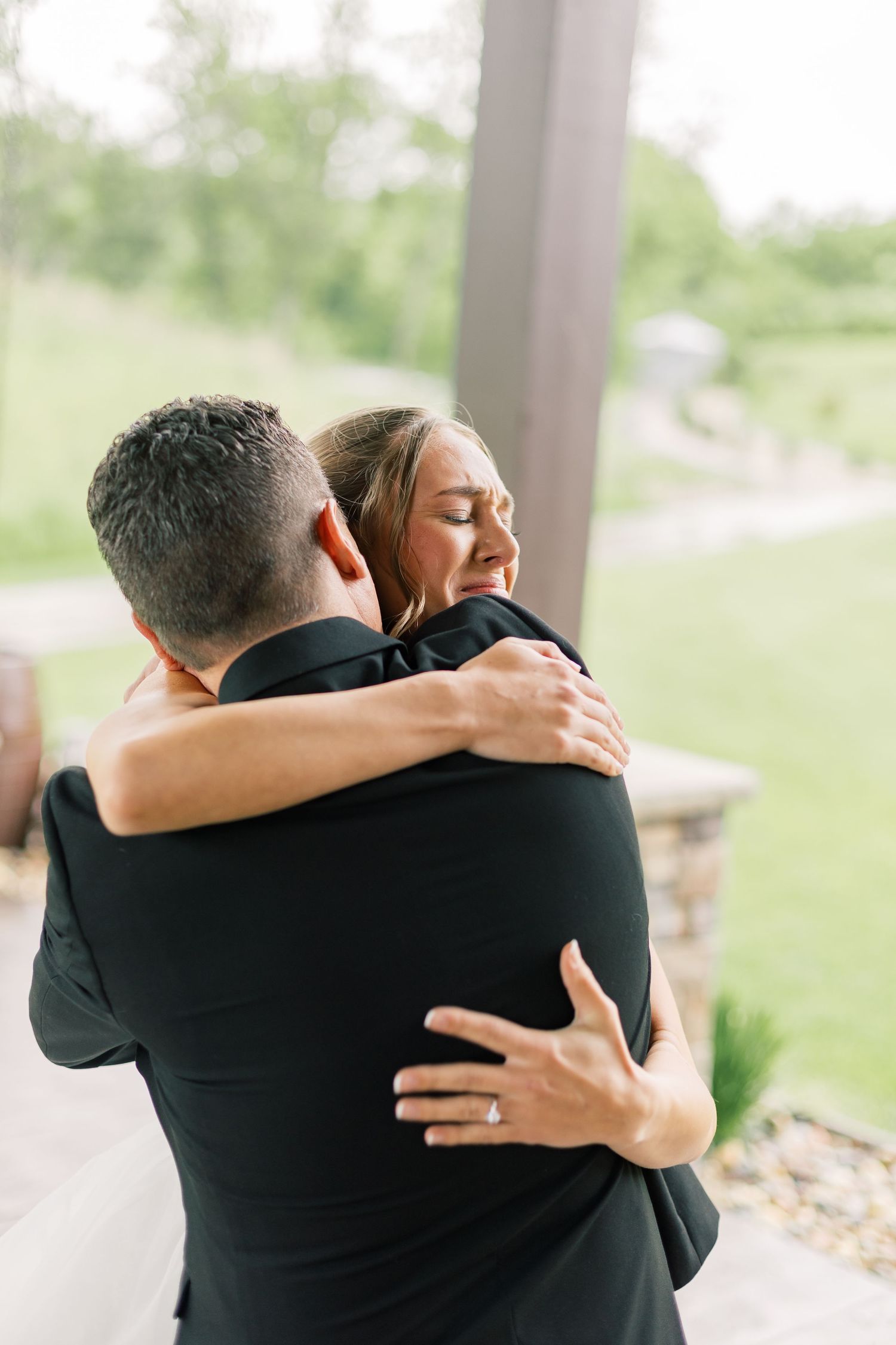 A tender embrace between a couple on their wedding day, with soft natural lighting and greenery in the background.