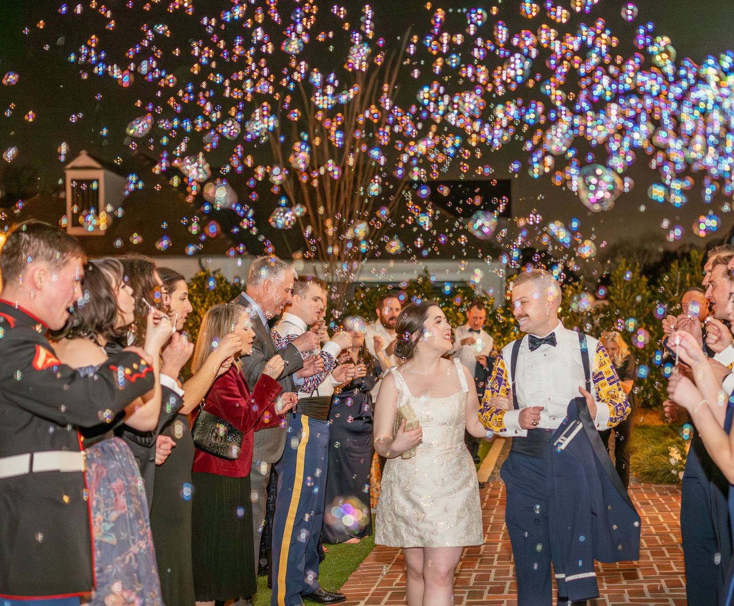 Celebration at an outdoor wedding reception with string lights and guests clapping under a magical evening sky.