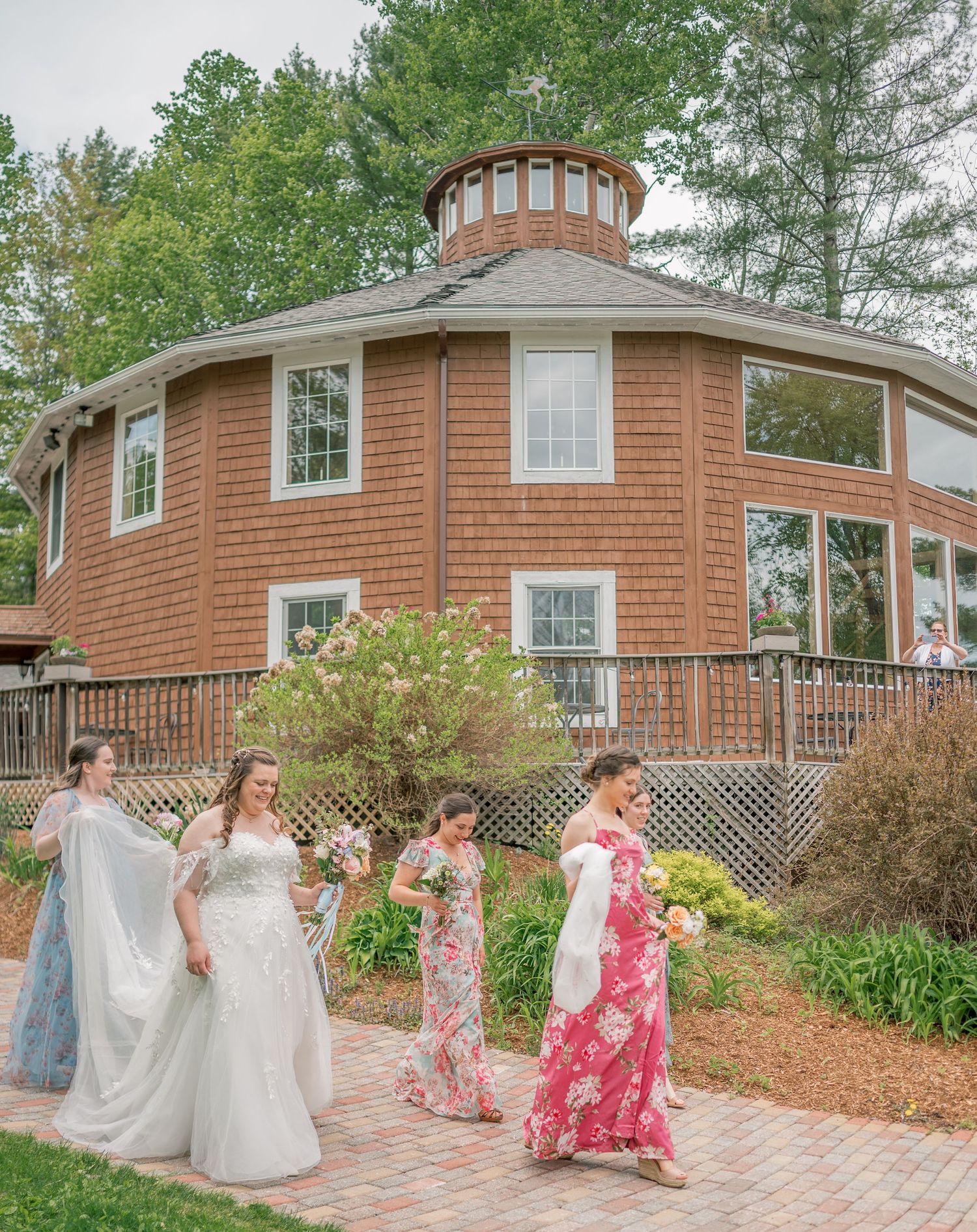 A group walks along a brick path outside a unique circular wooden house with cedar siding and a cupola on top.
