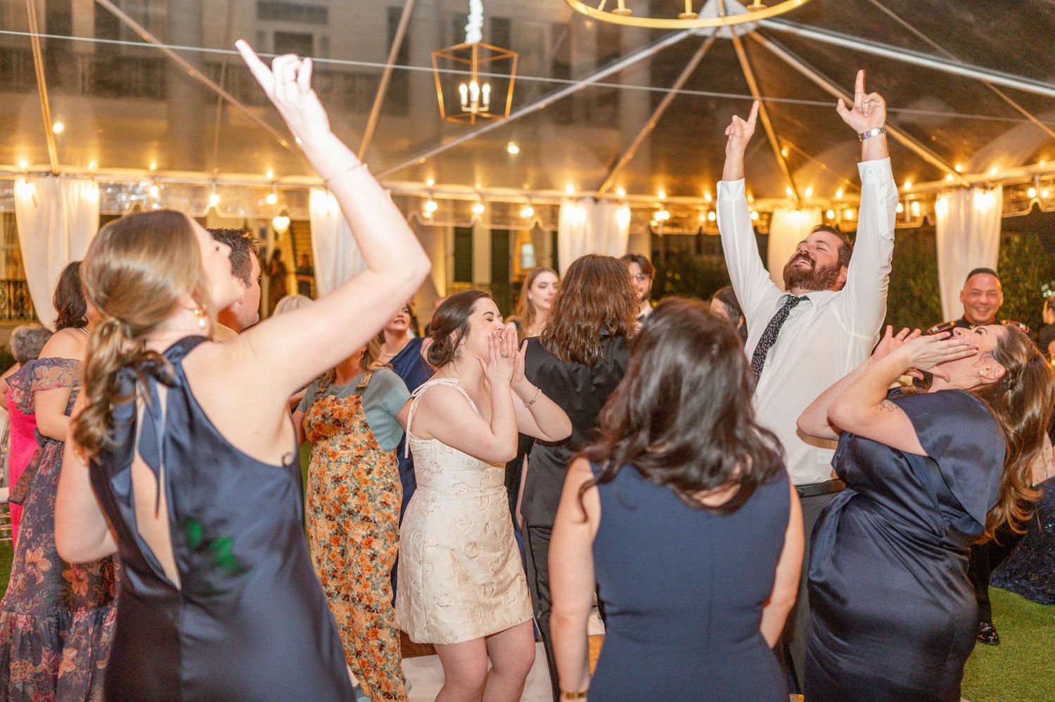 Wedding guests dance together on a dimly lit dance floor during an evening reception celebration.