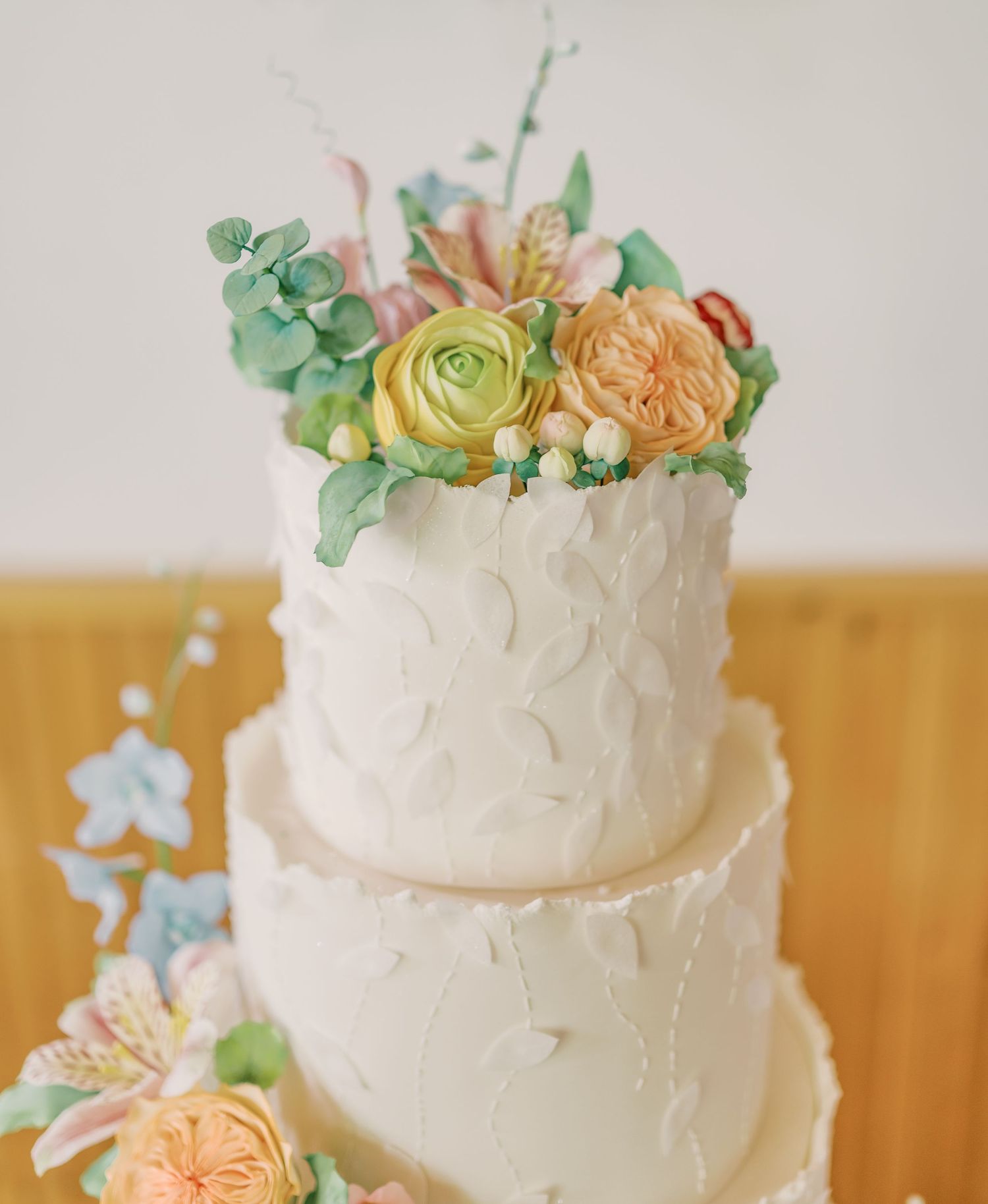A close-up view of a white frosted wedding cake decorated with delicate peach roses and green succulents on top.