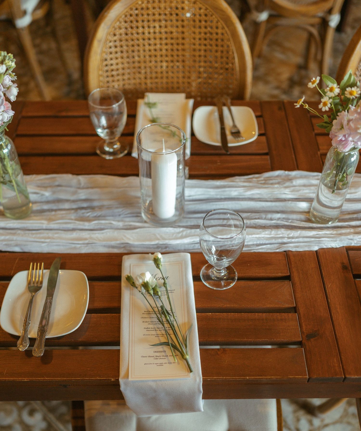 Elegant rustic wedding reception table setting with white linens, wine glasses, and delicate floral centerpieces.