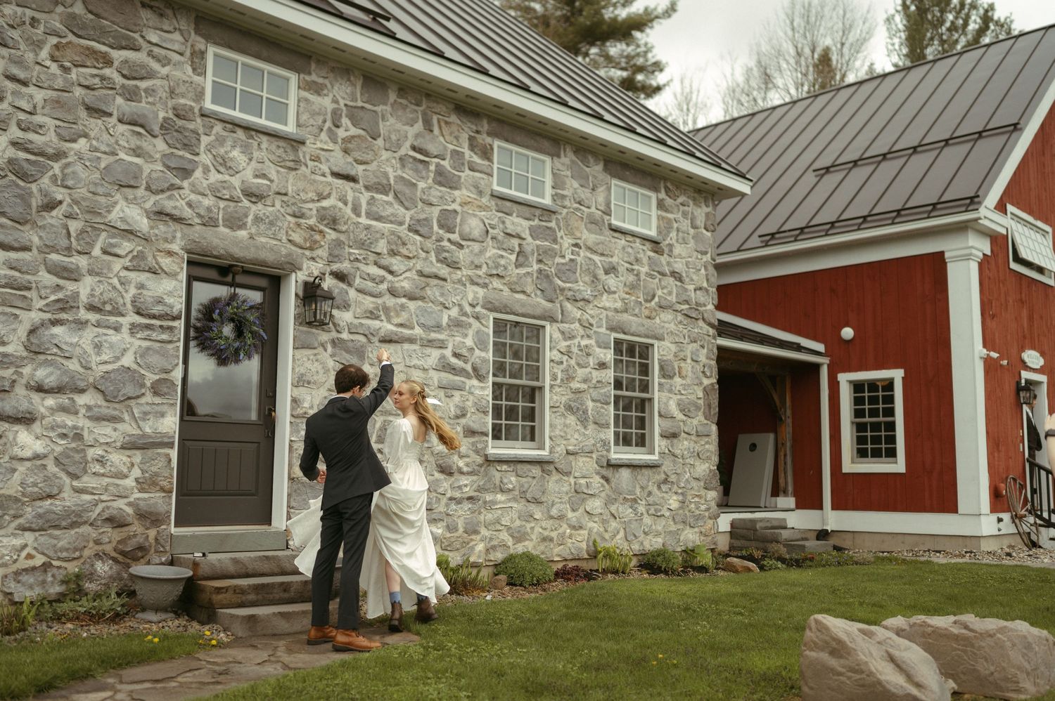 A panoramic view of stone buildings with red trim and metal roofs nestled against a stone wall in a rural setting.