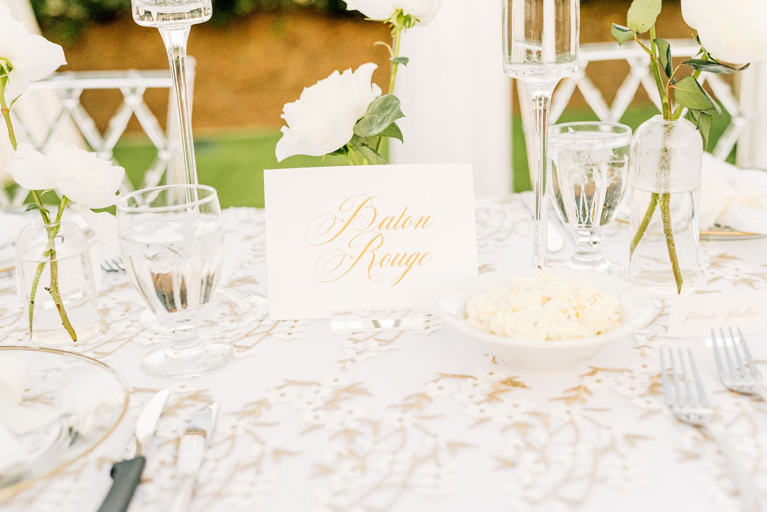 Elegant wedding table setting with white lace tablecloth, crystal glasses, and delicate calligraphy place card.