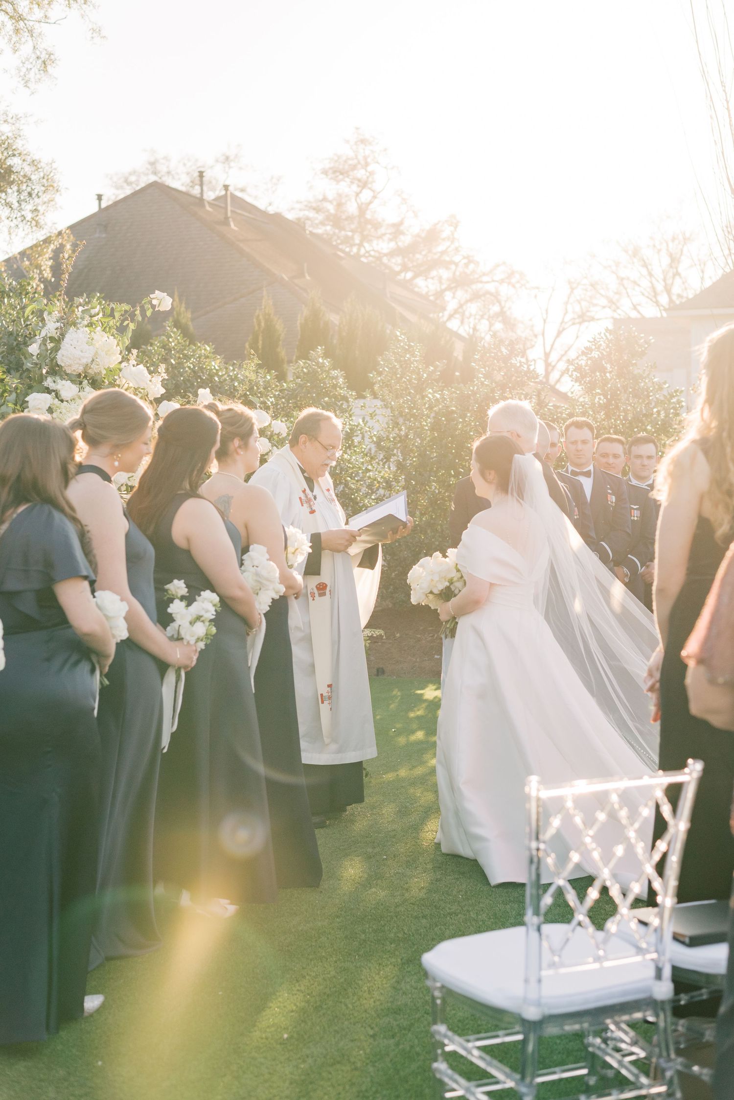 A romantic outdoor wedding ceremony with bridesmaids in navy dresses and a white arch at golden hour.