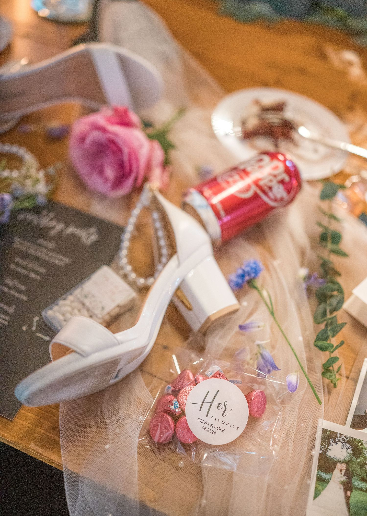 White wedding heels with floral decor and personalized tags arranged on a wooden surface for wedding detail photos.