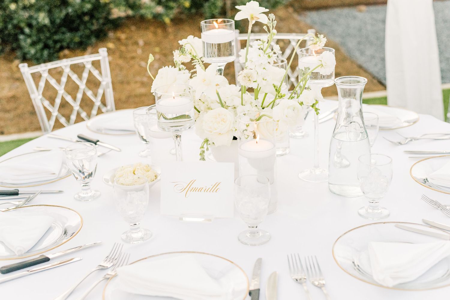 Elegant white table settings with crystal glassware and floral centerpieces at an outdoor wedding reception.