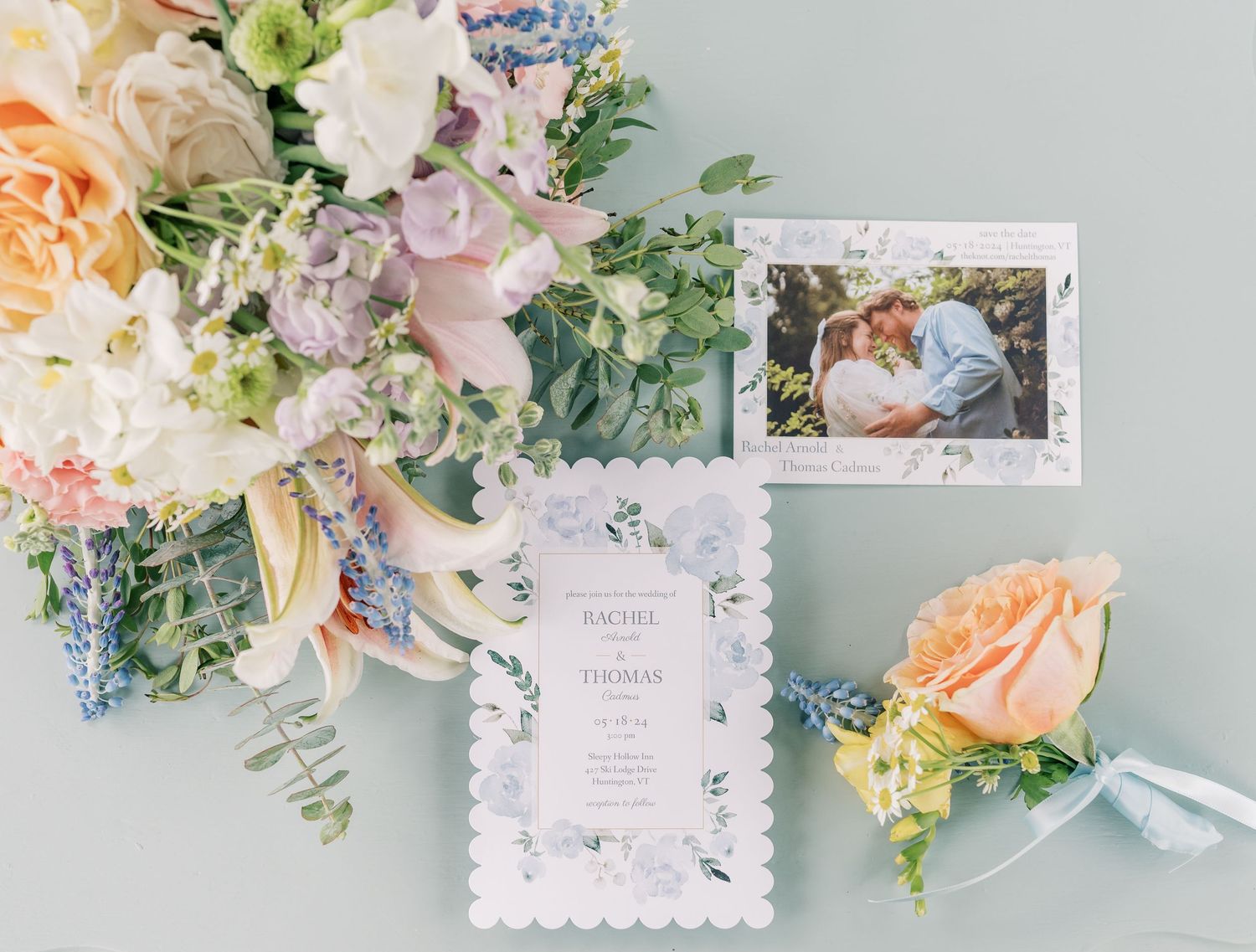 Wedding invitation suite with pastel floral arrangements and delicate stationery on a soft blue background.